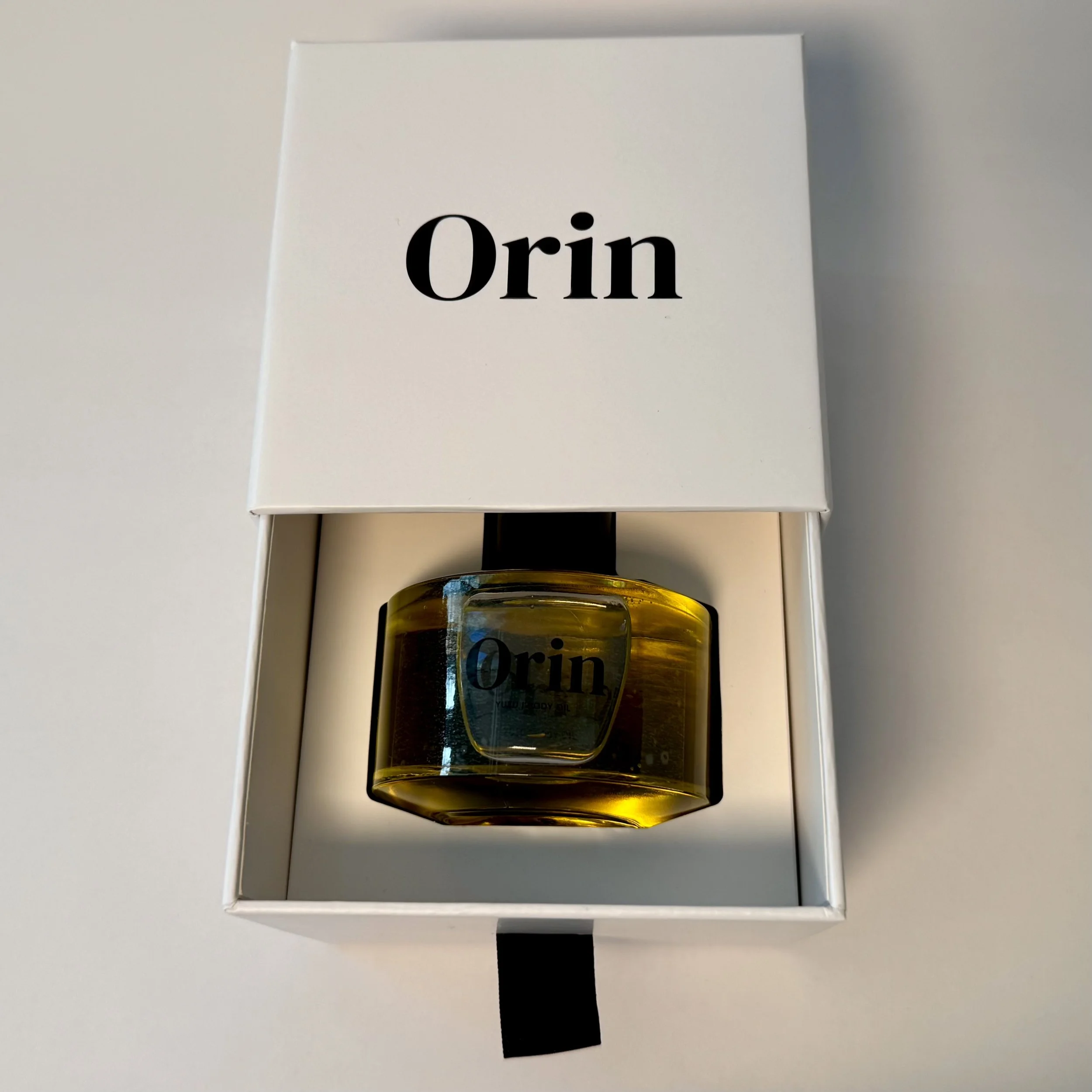 100ml Orin Yuzu Body Oil securely nestled in an open white luxury drawer box. This premium presentation highlights the high-performance botanical lipid blend, formulated to support a vibrant glow.