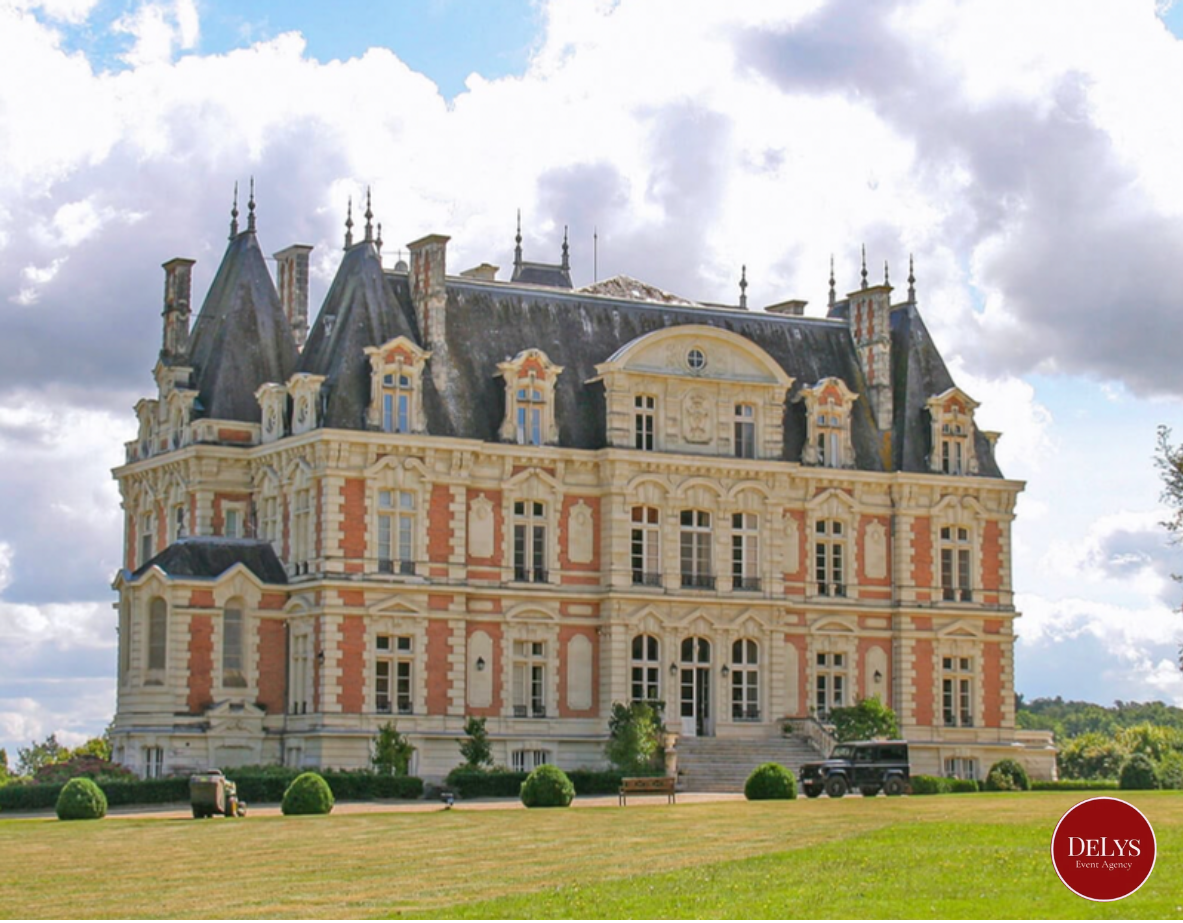 A large, ornate castle-like building with detailed architecture, multiple tall pointed towers, and a surrounding lawn with bushes in front.