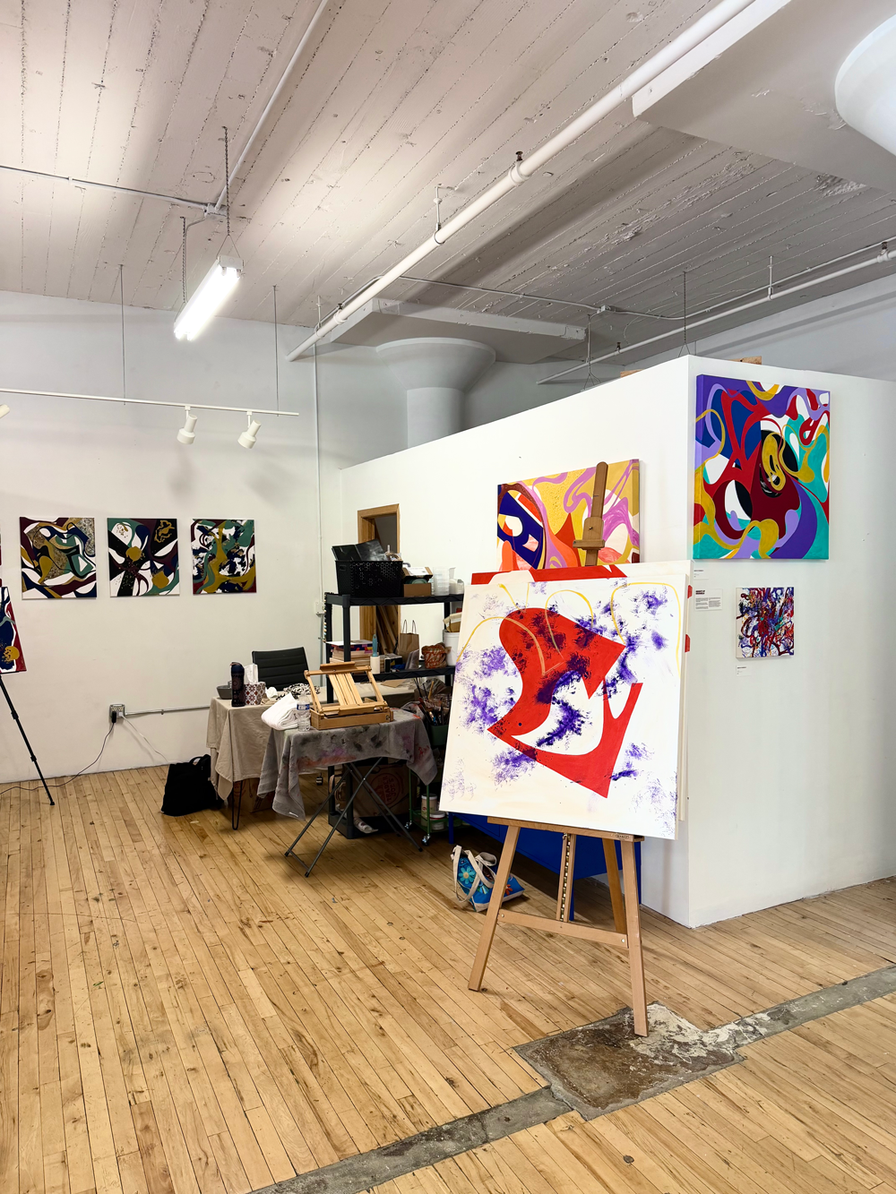 Interior view of contemporary abstract artist Nailah Ali's fine art studio, featuring oil and acrylic paintings on white gallery walls and an original canvas on a wooden easel at the Northrup King Building in Minneapolis.