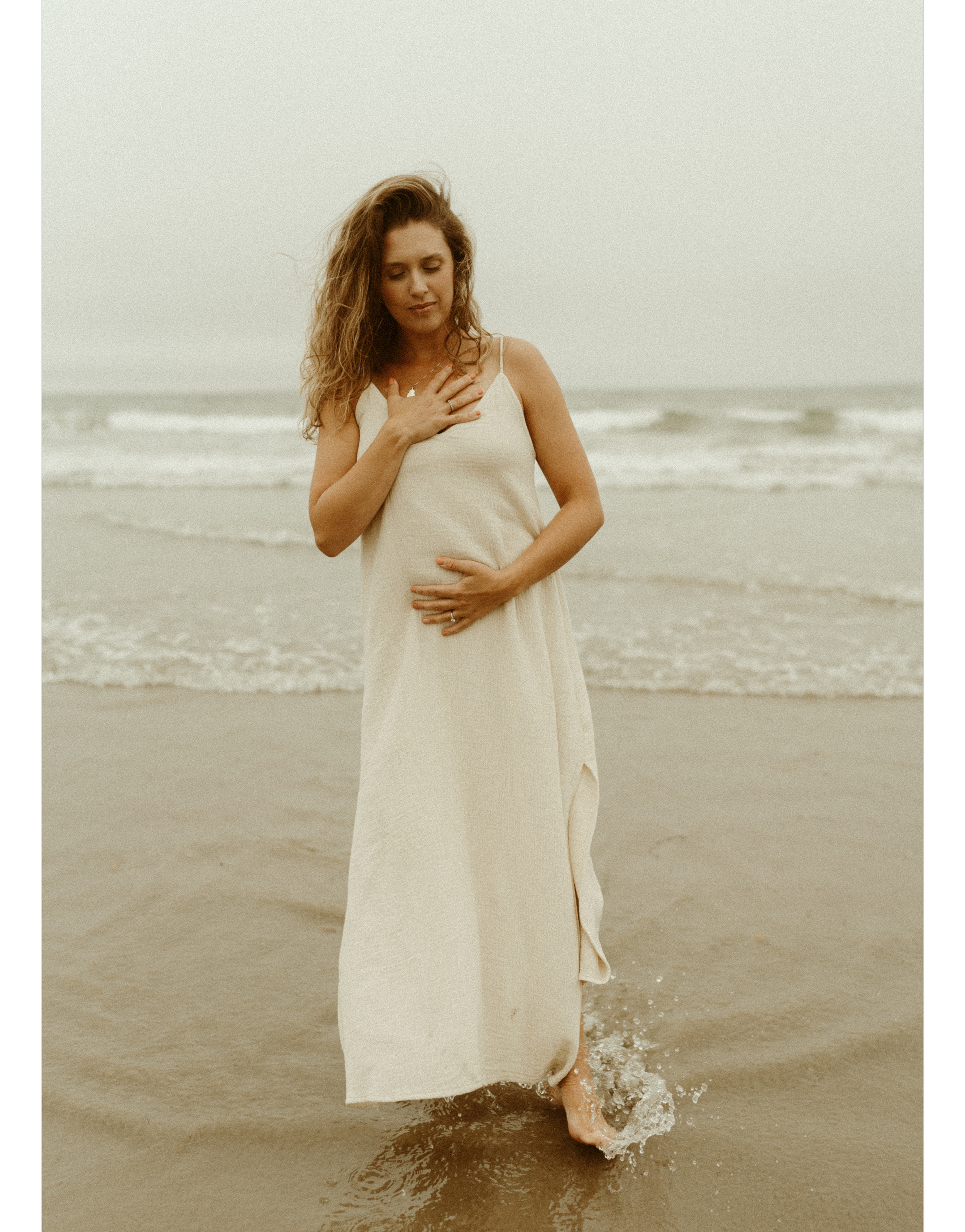 A woman in a white dress walking in the ocean waves at the beach.
