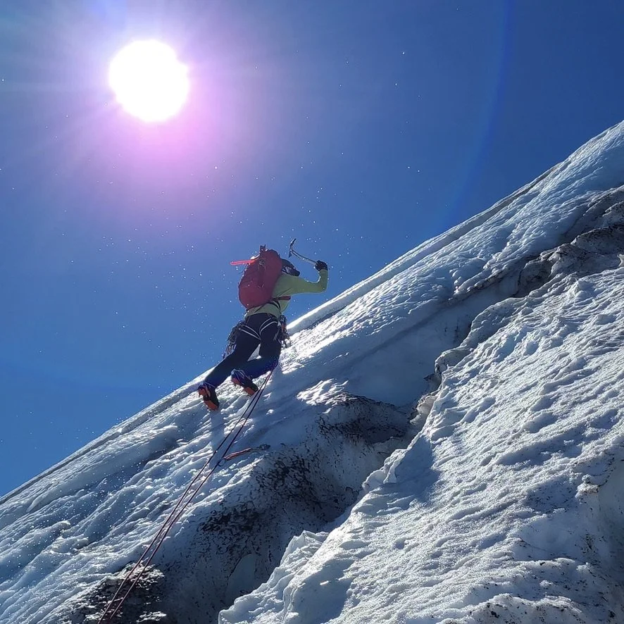 Mountaineer climbing a snow-covered icy slope on a clear sunny day with blue sky.