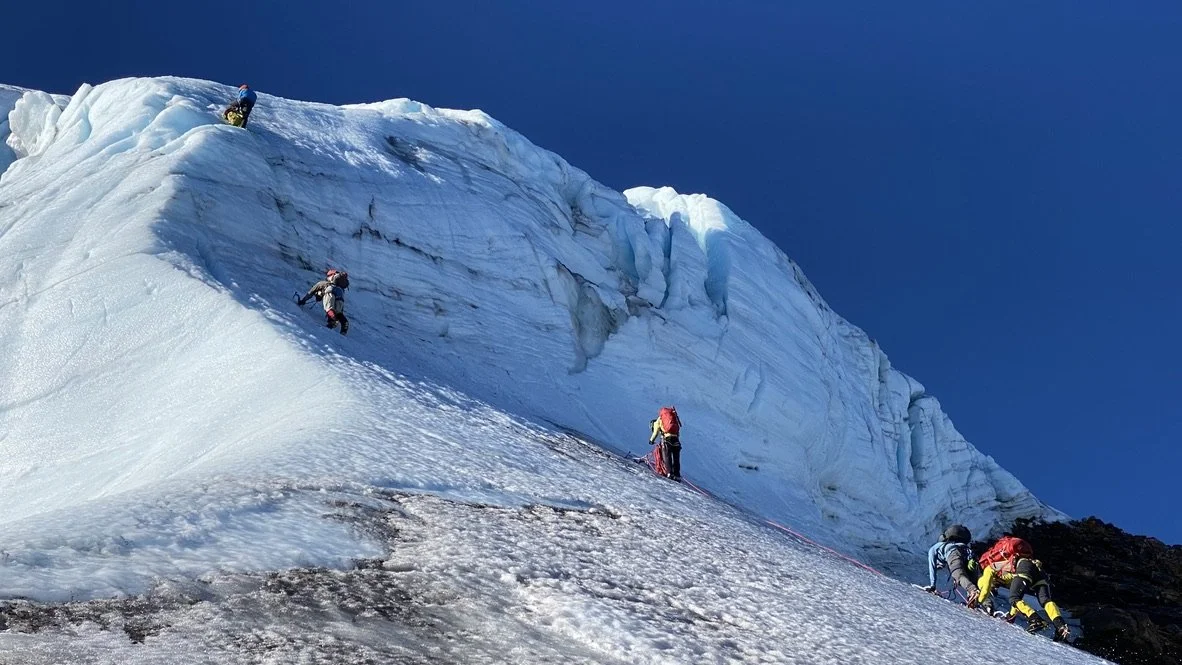 A group of climbers ascending a steep, icy glacier against a clear blue sky.