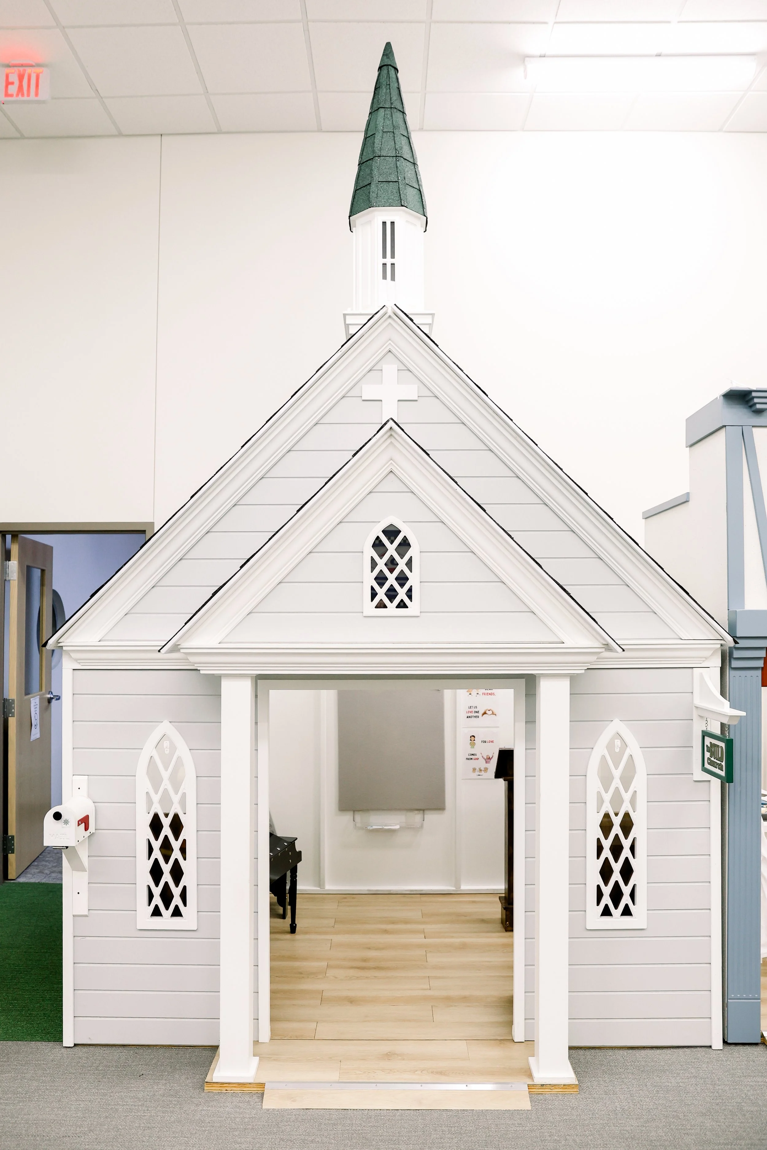 Small white and gray indoor playhouse resembling a church with a steeple, windows, and a cross on the front