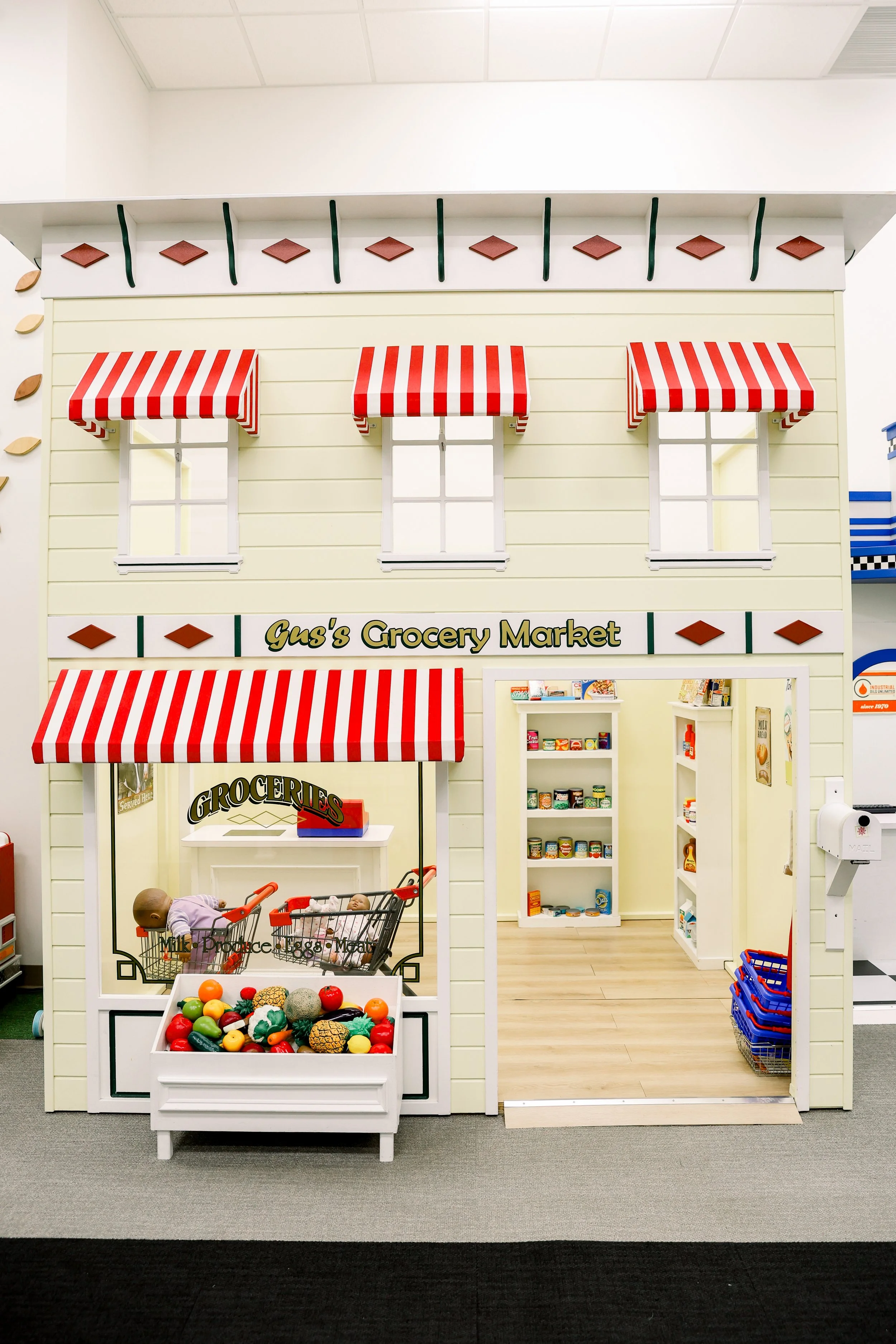 Miniature toy grocery store with striped awnings, shelves of food, and a sample produce display outside.