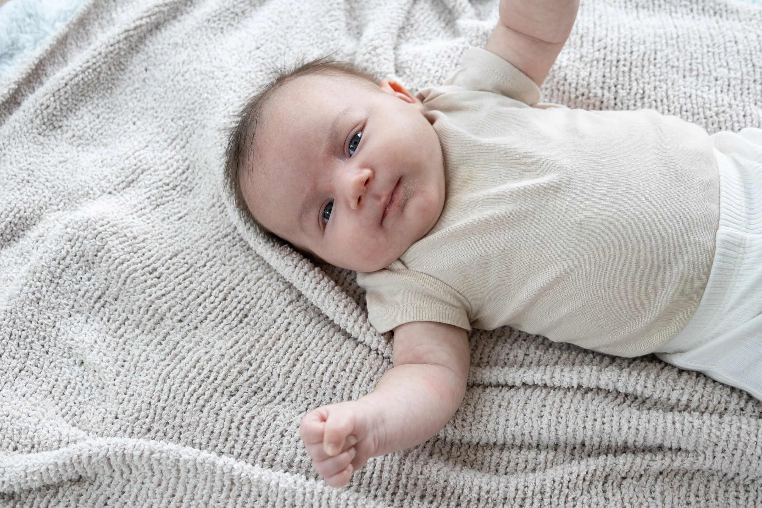Baby stretching out on a blanket in living room in home in Huntington Indiana photographed looking at the camera with hands out