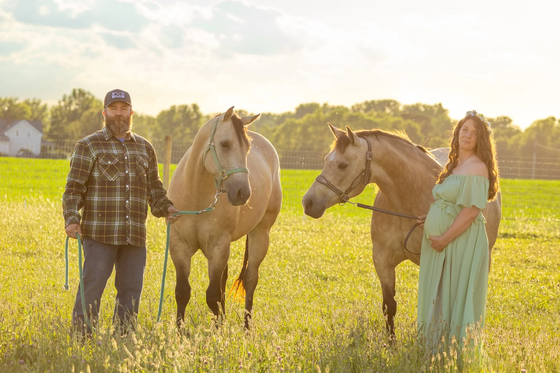 husband and expecting wife with two horses in a grassy farm field countryside setting photographed at sunset in Indiana