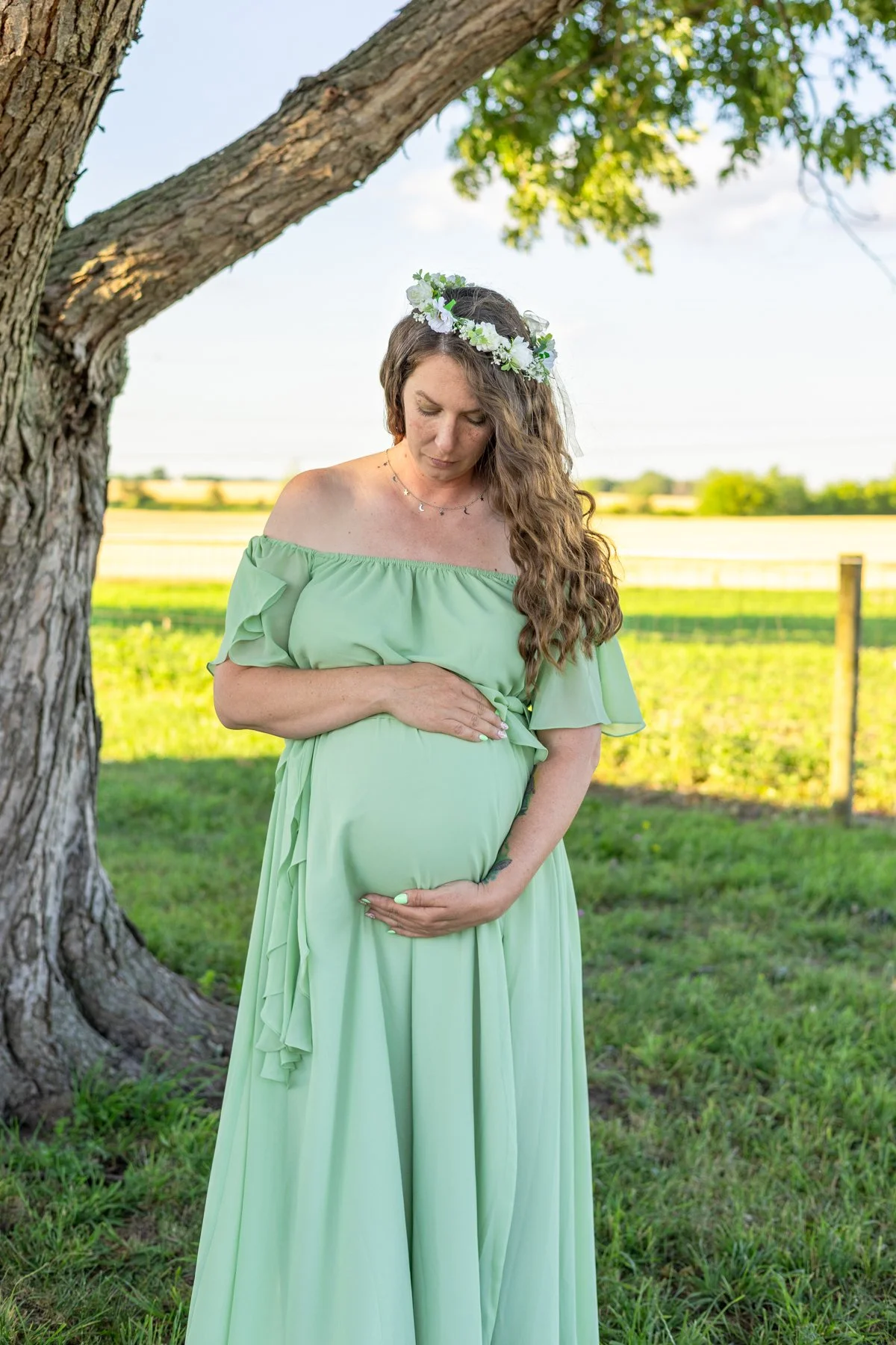 Maternity photo taken under a tree with farmland in the background