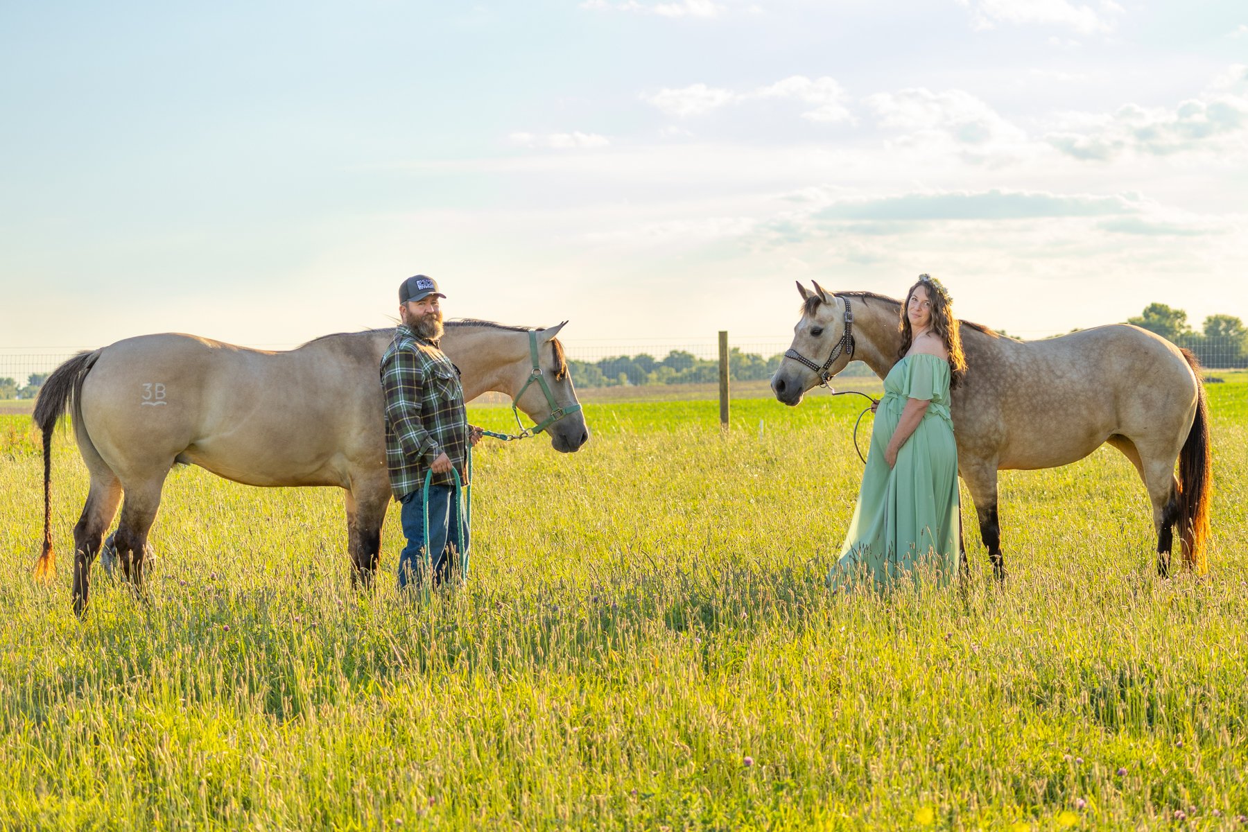 Two horses and husband and wife standing next to each horse facing each other at sunset time in a field in Indiana