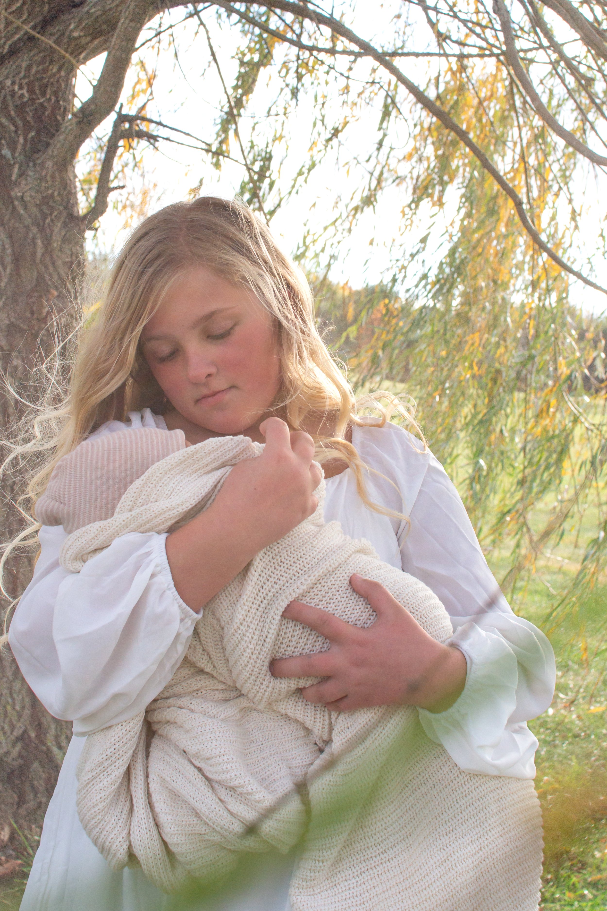 Newborn being held by big sister under a willow tree photographed in Huntington Indiana
