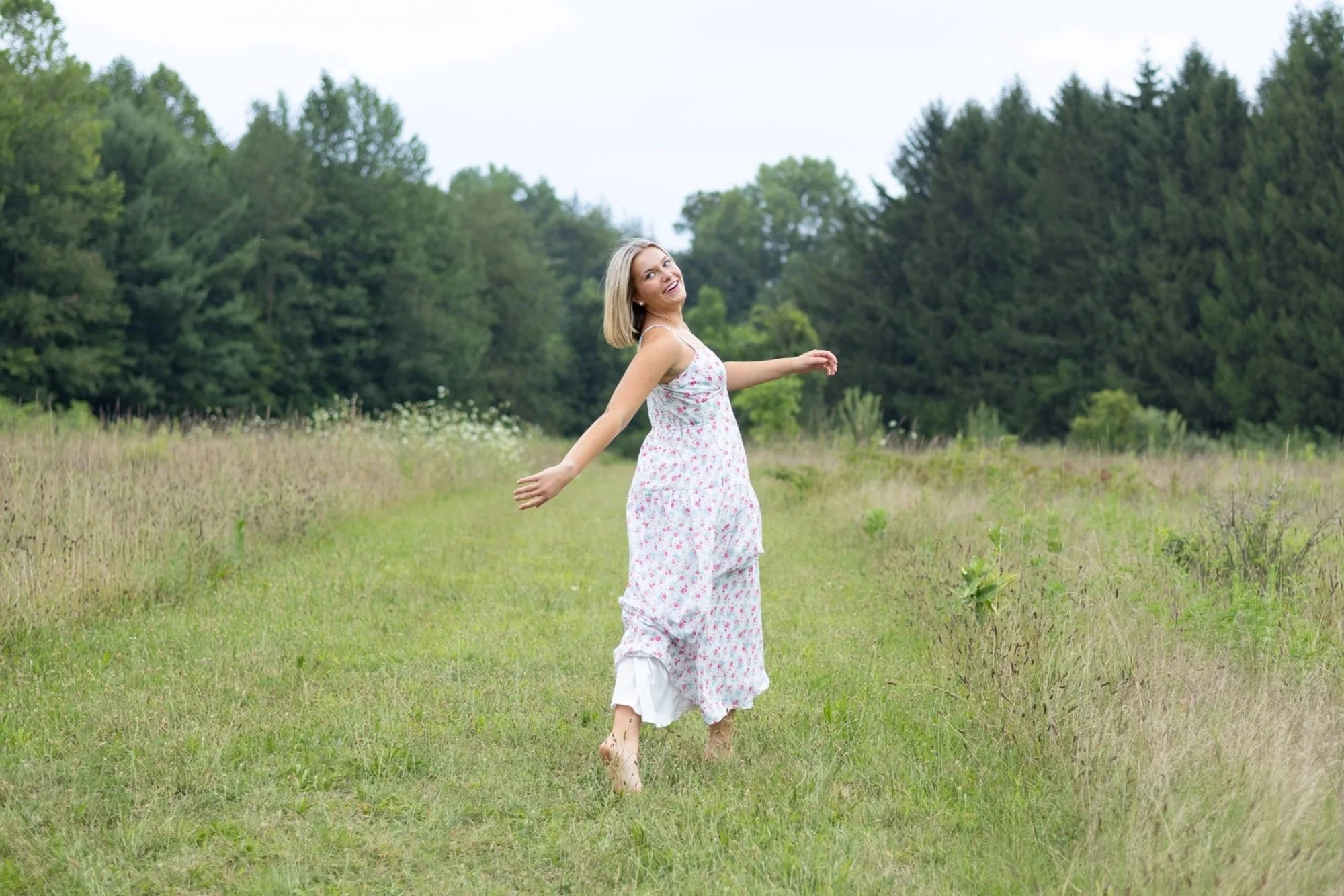 high school senior walking through the grass with trees behind her in Huntington by a photographer using candid and meaningful style