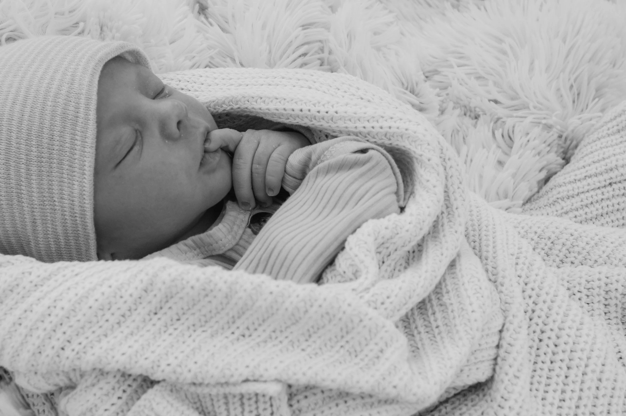 Newborn photographed in black and white on soft blankets with a hat on and is in a candid moment in a Huntington Indiana park