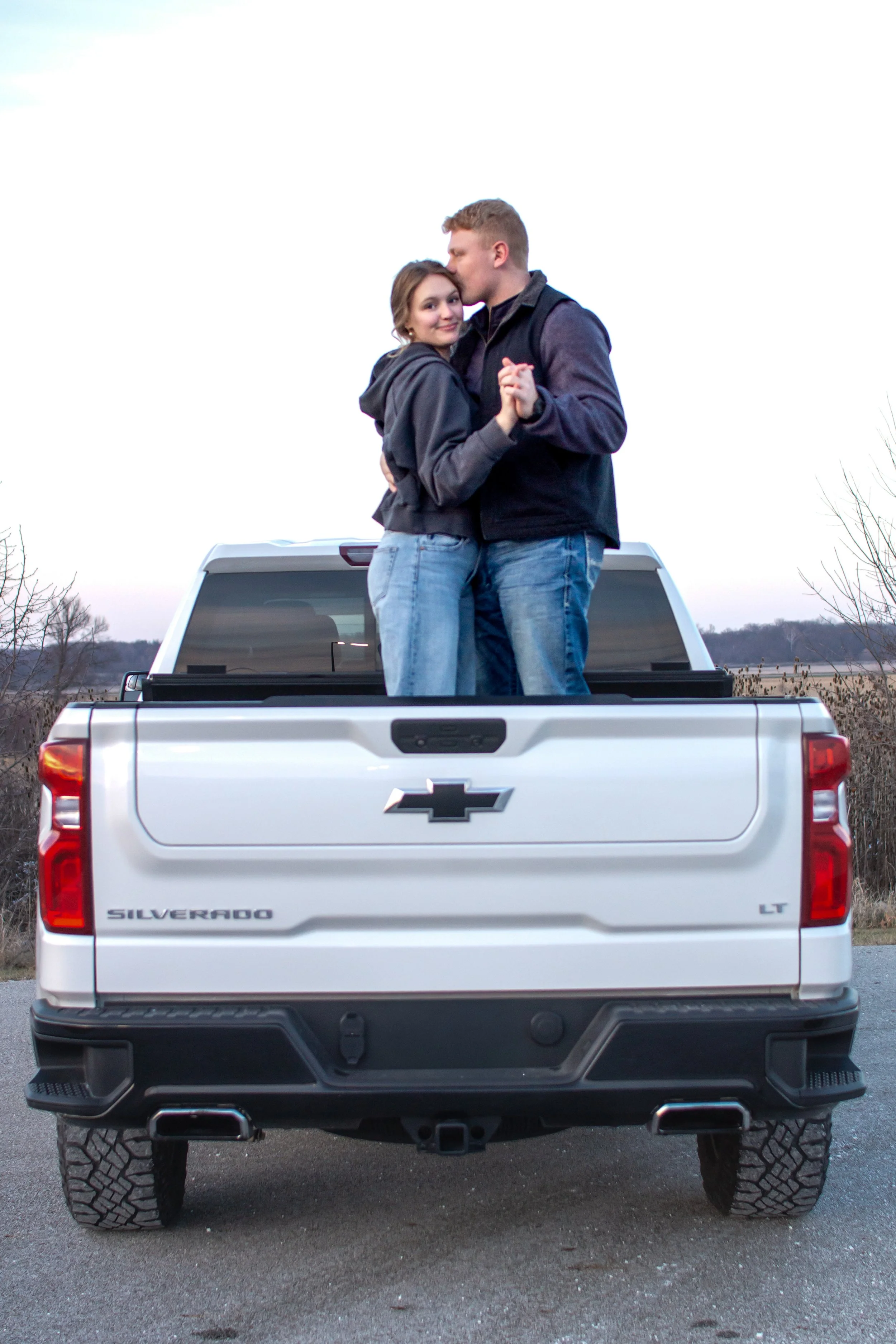 man and woman dancing in the back of a pick up truck and photographed at a park in fort wayne