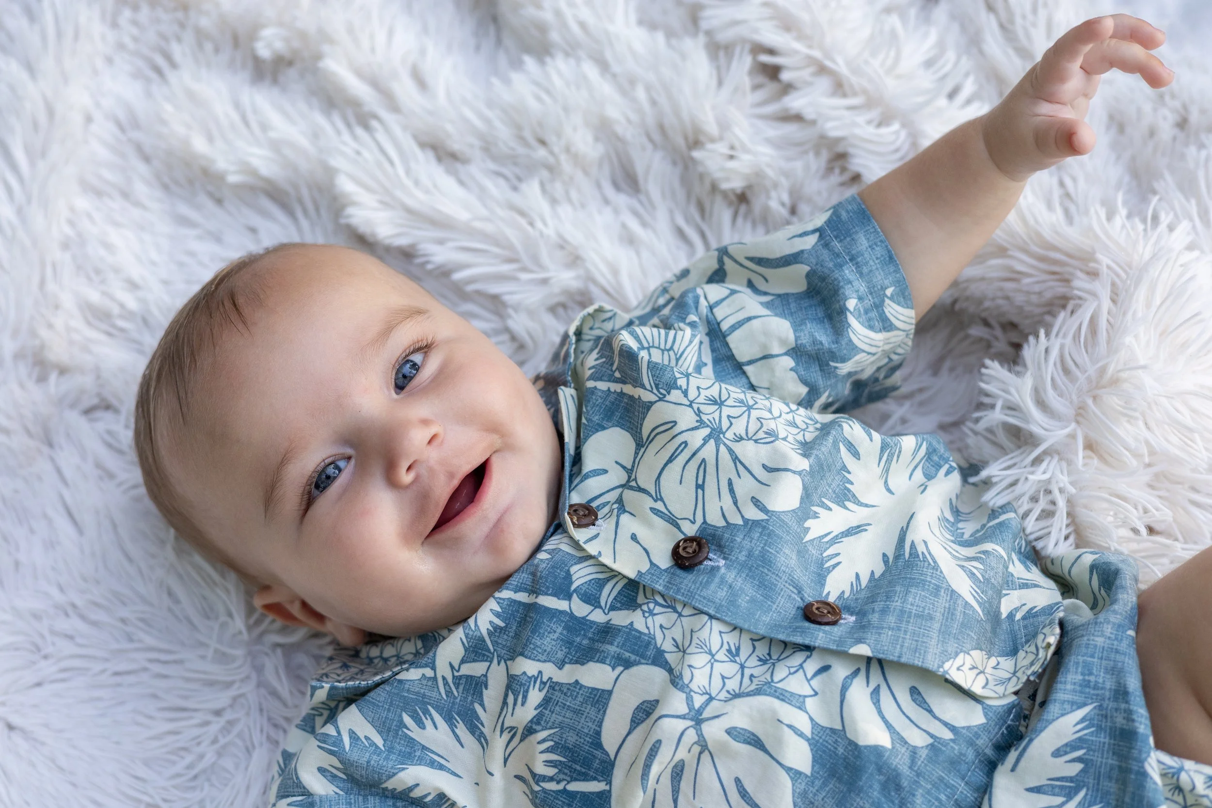 Baby laying on a blanket looking up at the camera with big blue eyes and smiling photographer captured a special candid moment