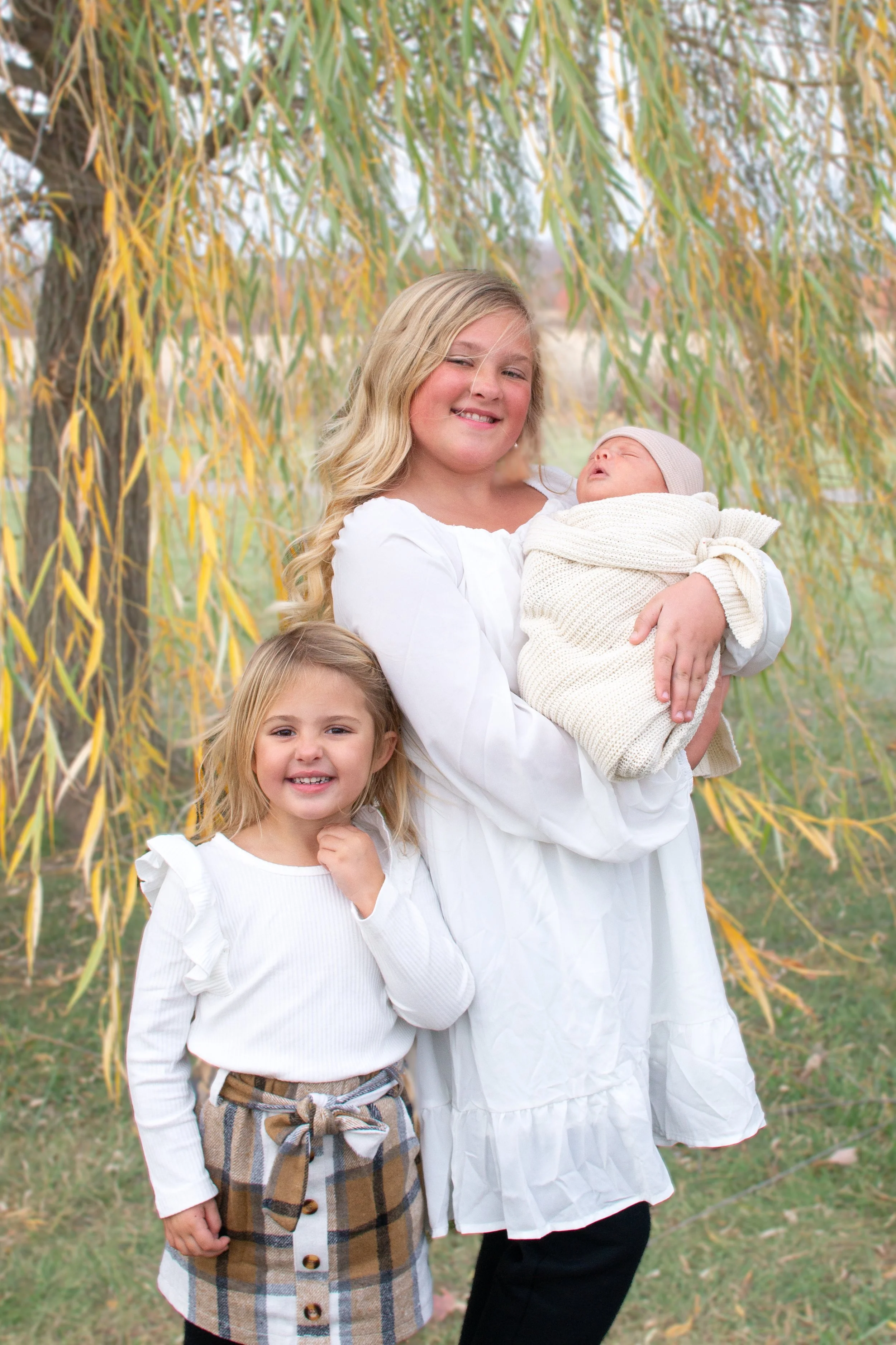 Newborn with sisters photographer under a willow tree in Huntington