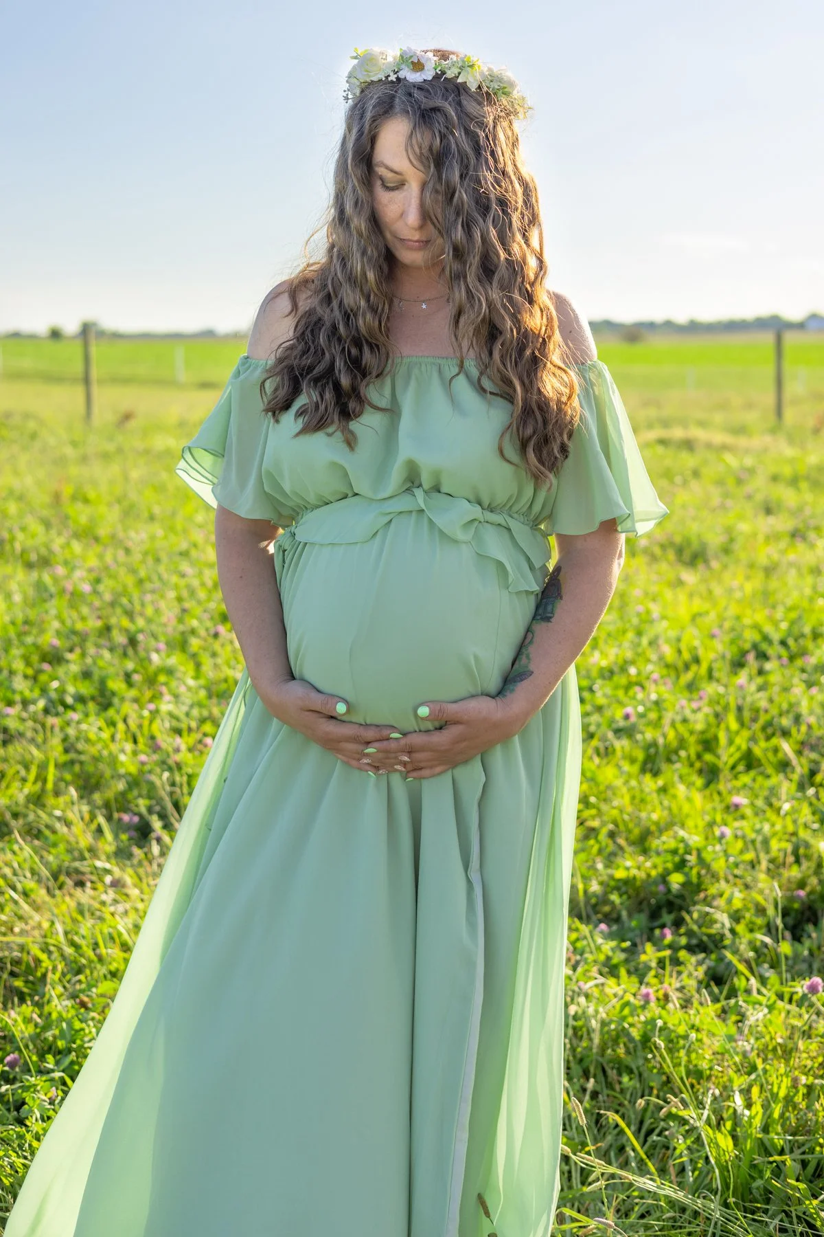 Maternity image of expecting mom wearing green dress with flowers in hair in a farm field in northern Indiana