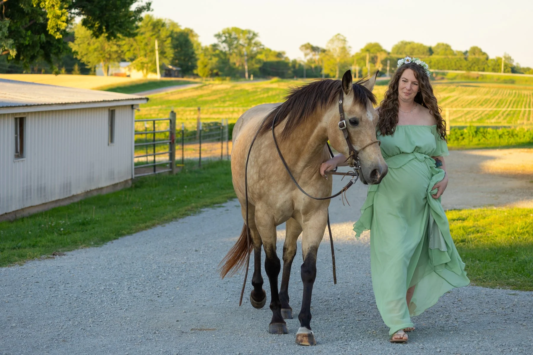 maternity expecting mom in a green flowy dress with flowers in her hair walking next to a horse at a farm in North Manchester, Indiana