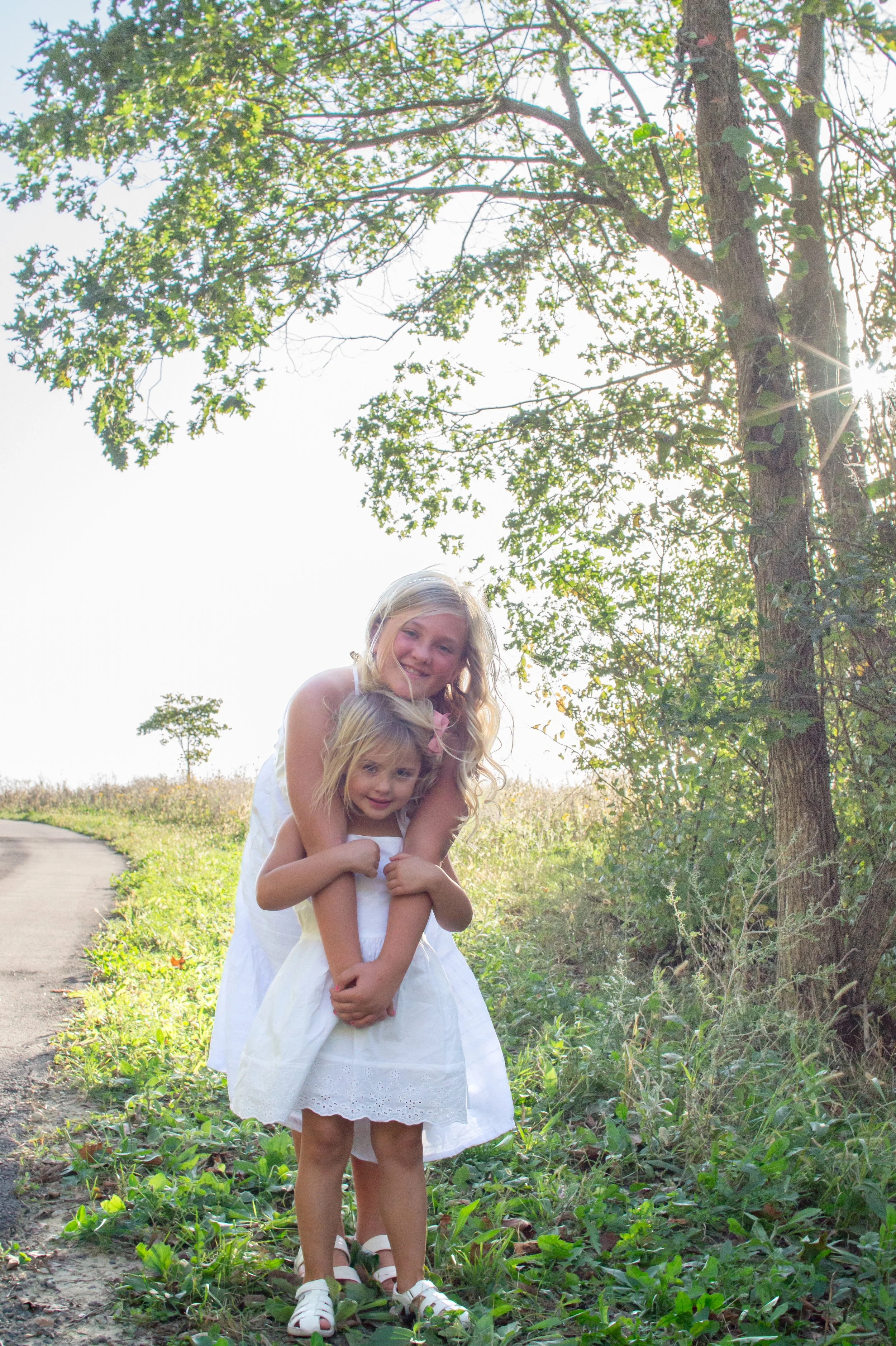 Sisters hugging under a tree with the sun behind them in Huntington taken by a family photographer