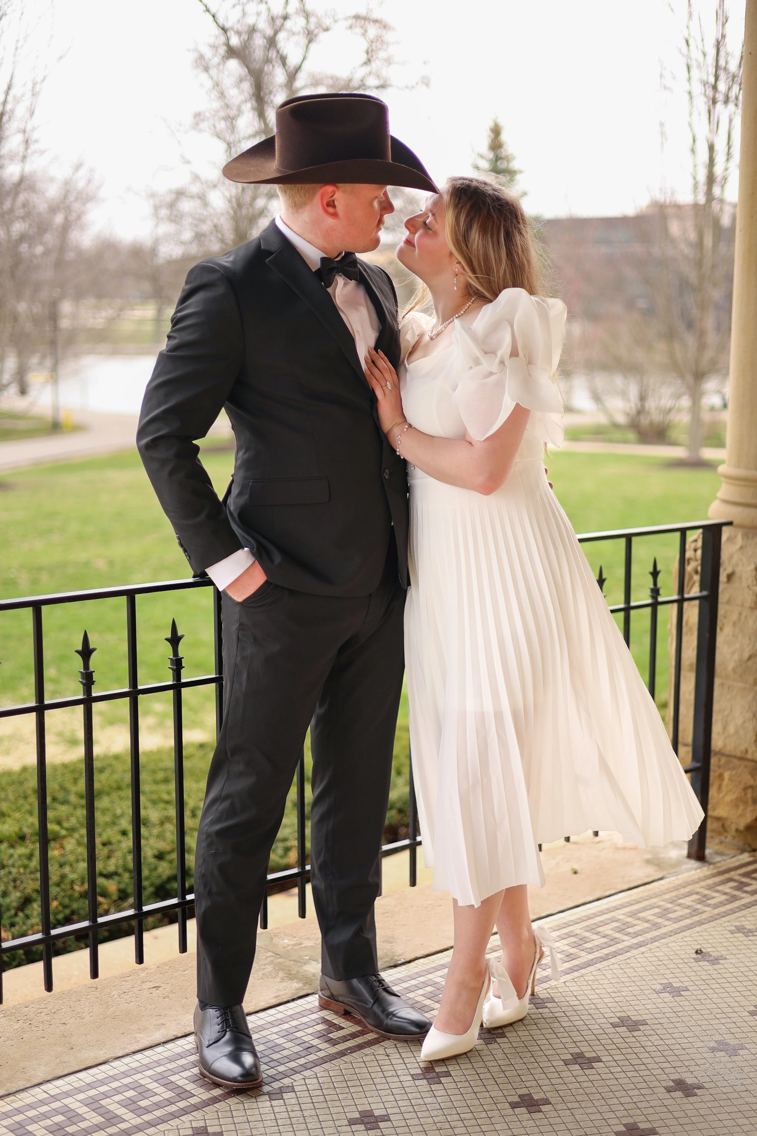 Man and woman wearing fancy clothes and a cowboy hat are close to each other and looking into each other eyes in a candid and natural way with natural light photographed at st francis in fort wayne