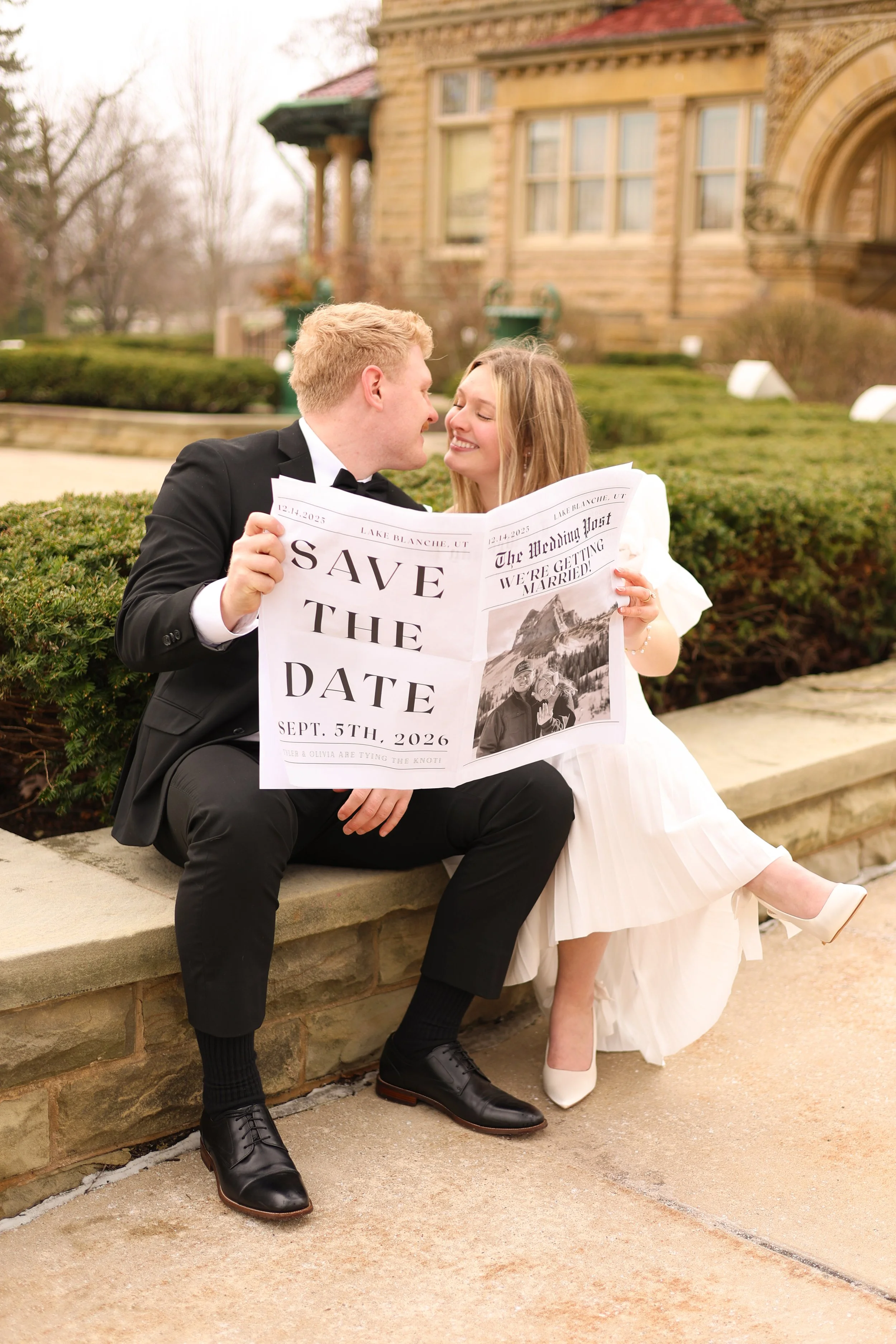 Man and woman looking at each other while holding a newspaper announcing their save the dates for the wedding photographed at st francis in fort wayne