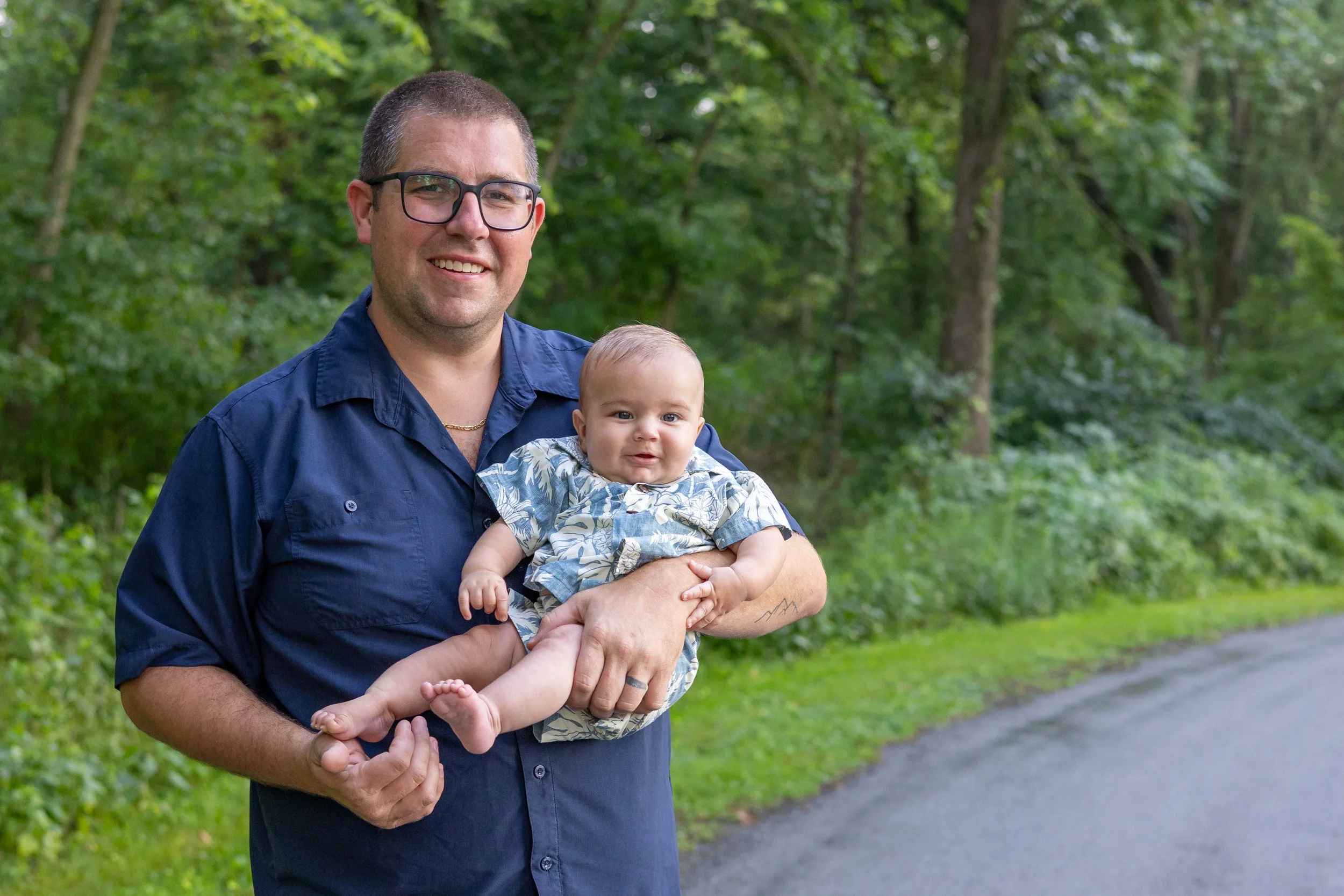dad holding baby and both are smiling at photographer in park in Huntington