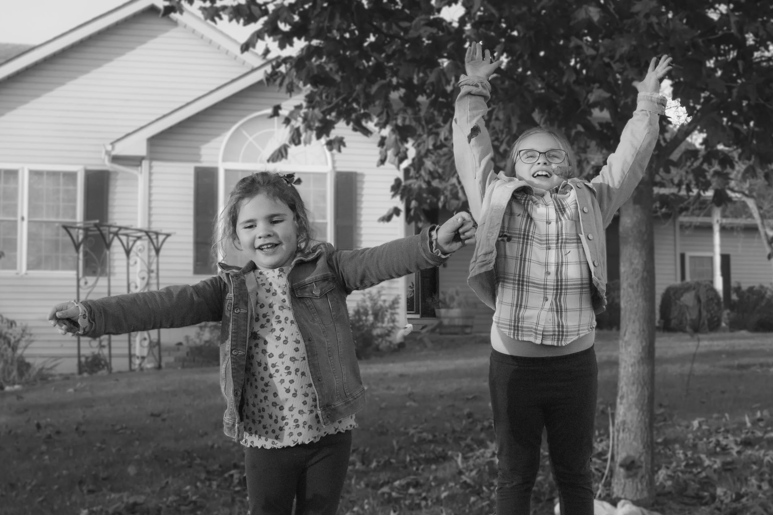 Sisters throwing fall leaves in the air photographed in black and white at Huntington Indiana