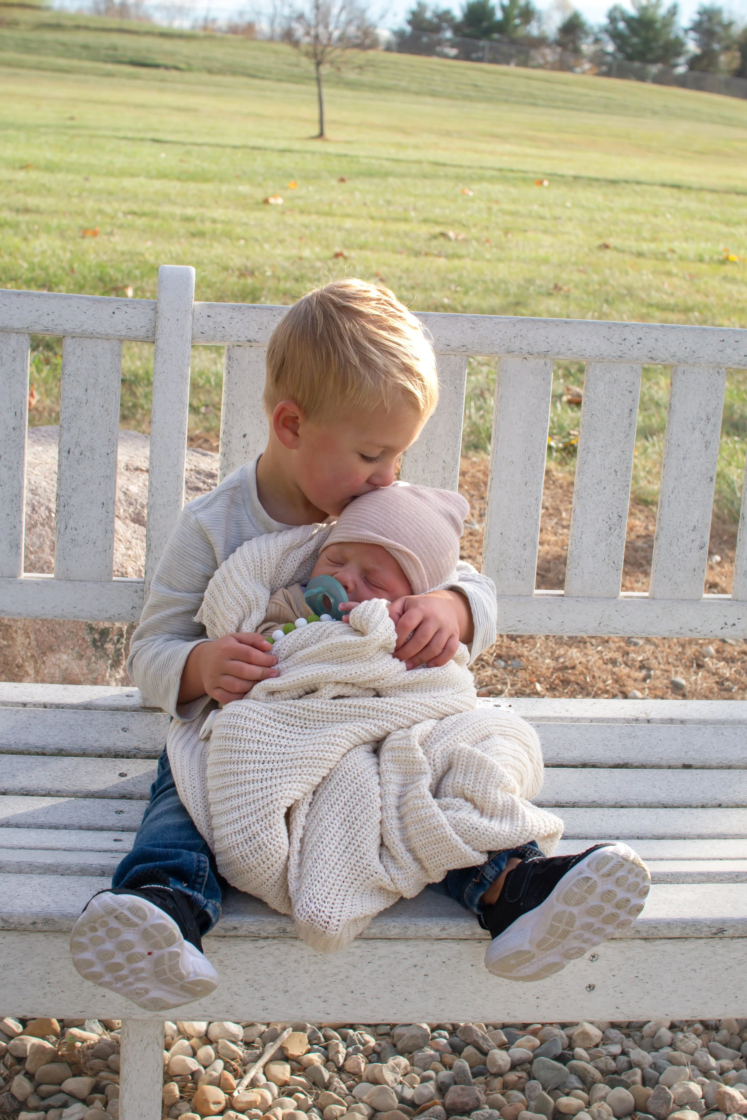 Newborn and brother snuggling on a bench at a park in Huntington Indiana, photographer captured the brother kissing the baby on the head and is so meaningful