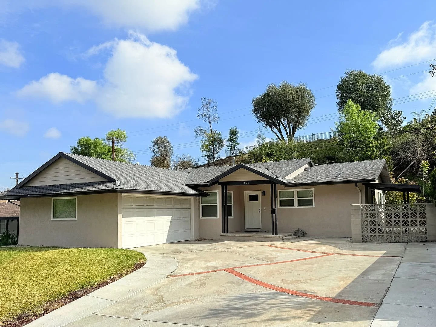 Exterior view of a single-story house with a two-car garage, grey shingles, a concrete driveway, and a small front porch under a partly cloudy sky.