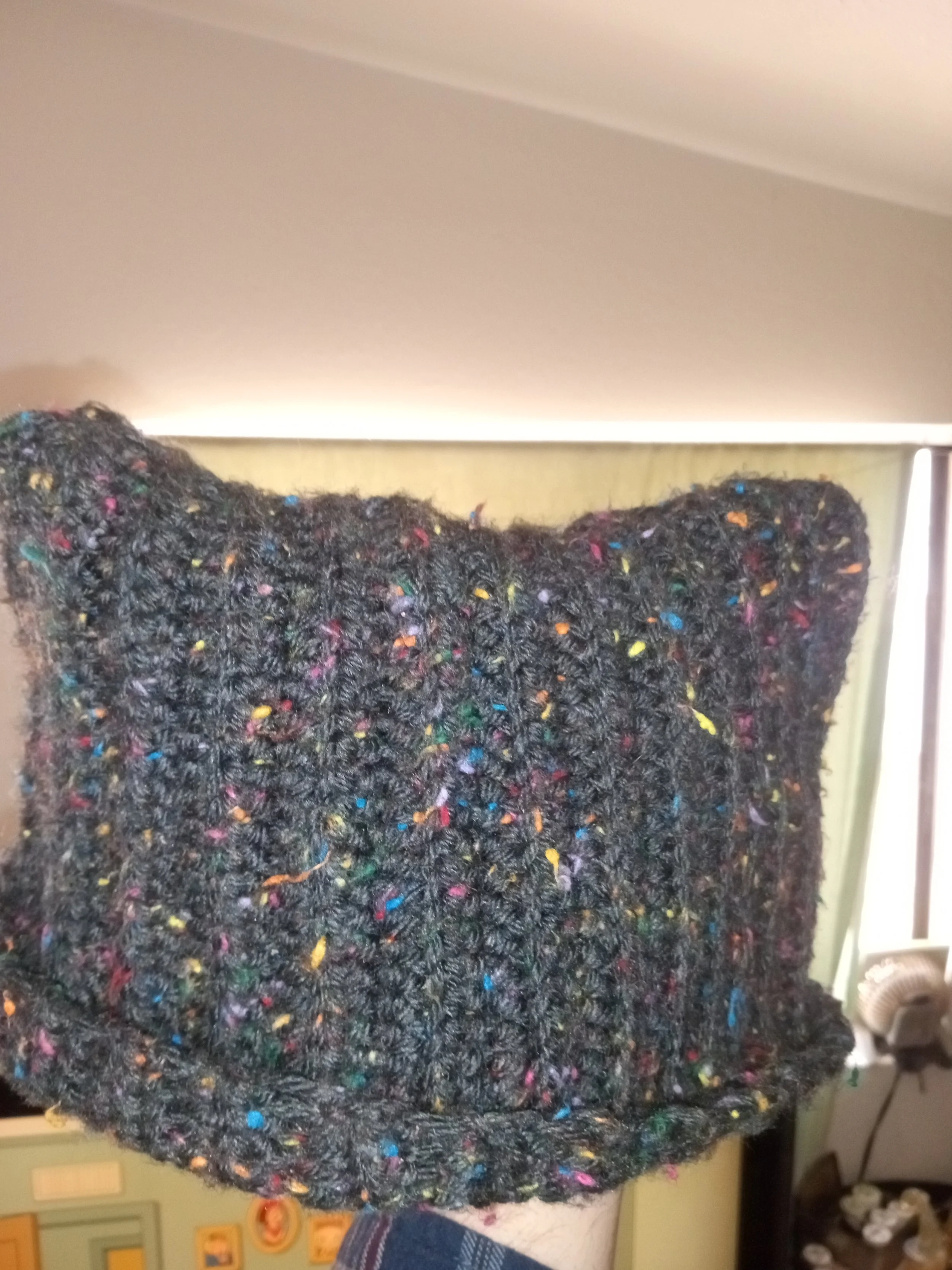 Close-up of a black, fluffy, textured object with colorful specks scattered throughout, set against a yellowish background.
Artisan, Handmade, Grass valley, nevada county, Kale Burnett, Crocheted Beanie, art.