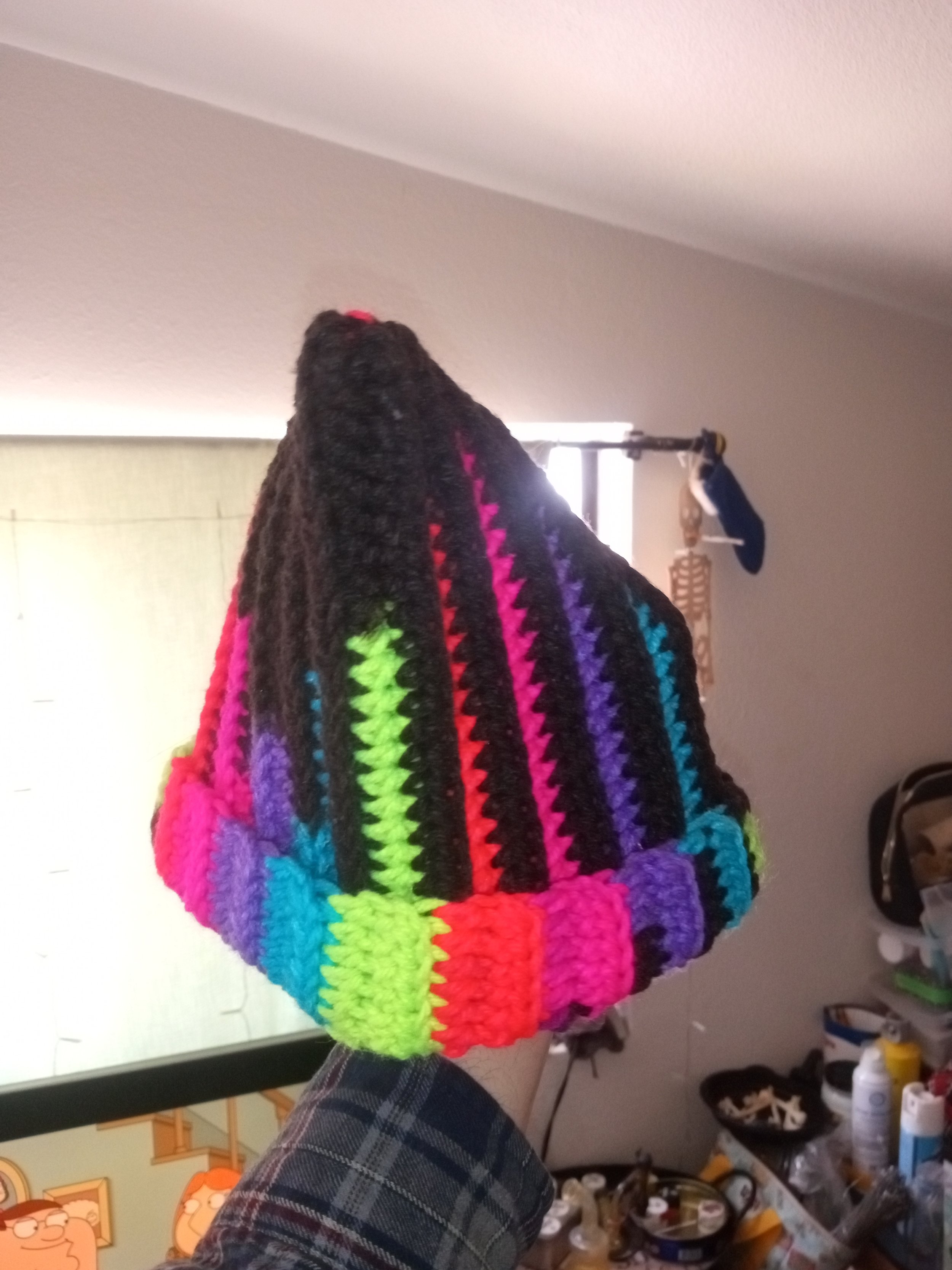 Close-up of a colorful, rainbow-striped, crocheted or knitted blanket or fabric, with a wall and some household items in the background.
Artisan, Handmade, Grass valley, nevada county, Kale Burnett, Crocheted Beanie, art.