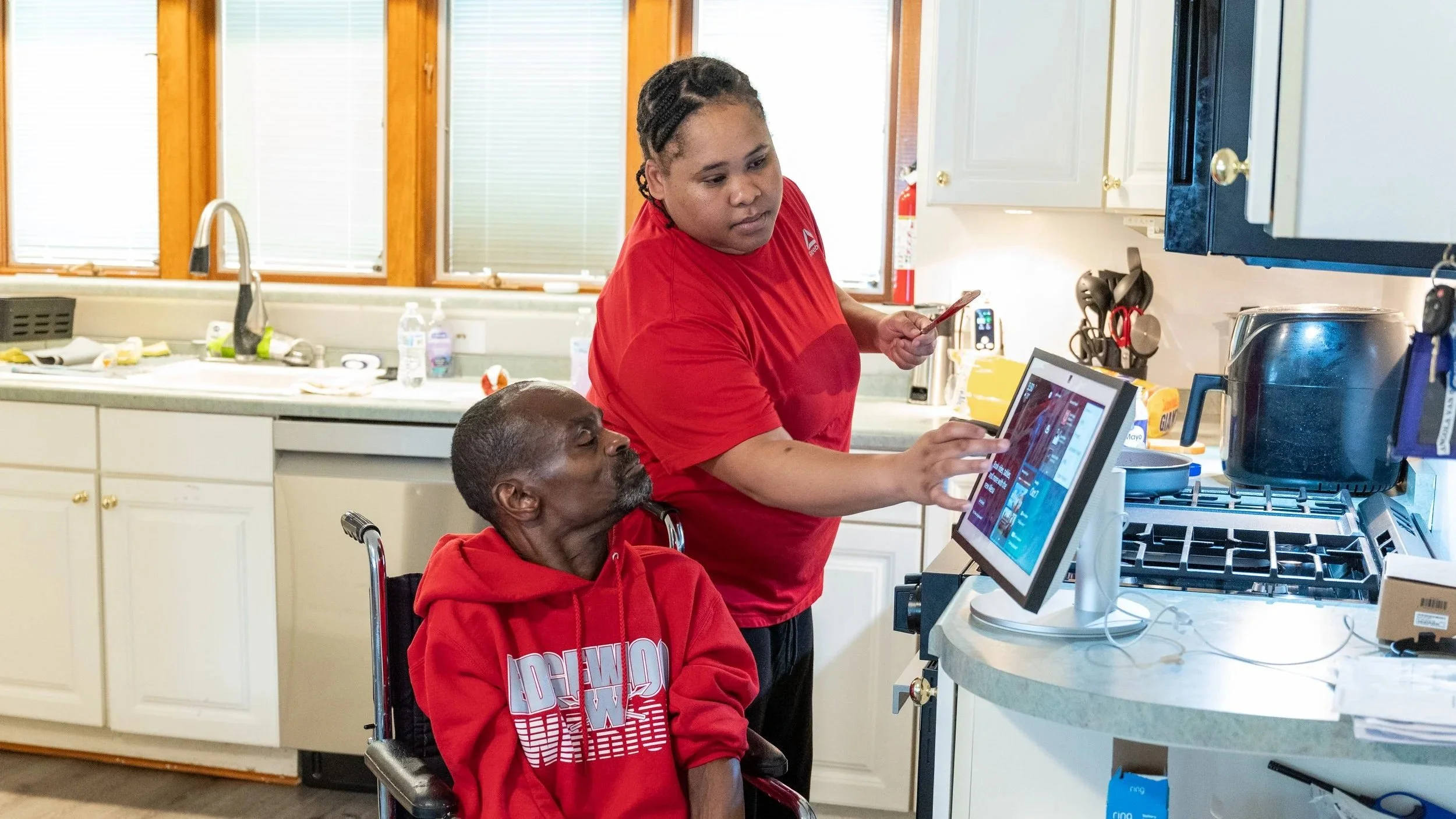 Adult services staff assisting a participant with meal preparation using adaptive technology in a home kitchen at the Epilepsy Center of Northwest Ohio, supporting independence and daily living skills.