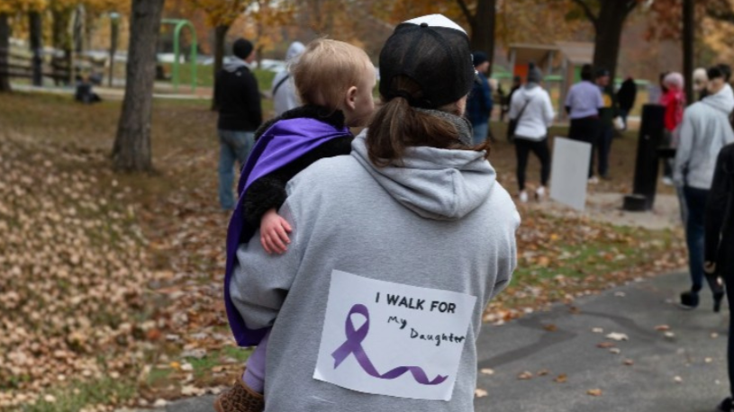 Parent carrying a child at the Carpe Diem Run/Walk with the Epilepsy Center of Northwest Ohio, wearing a shirt that reads “I Walk for My Daughter” in support of epilepsy awareness.