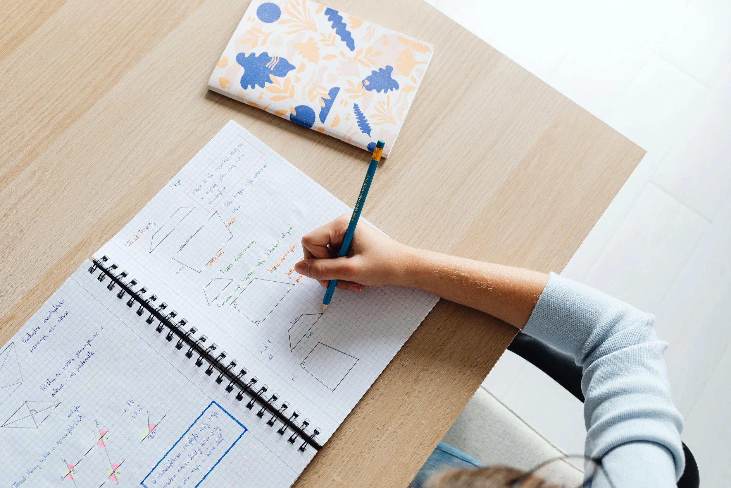 Close up image of a child's arm as they write geometric shapes and measurements in their grid notebook