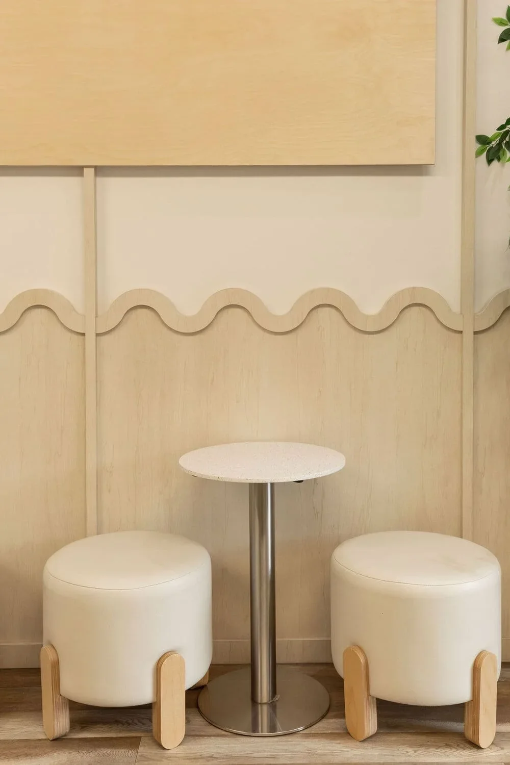 Coin tabourets du café Be Healthy Love Berry en Rive-Nord par Rübik Design : tabourets crème à pieds en bois, table ronde et mur à motif ondulé