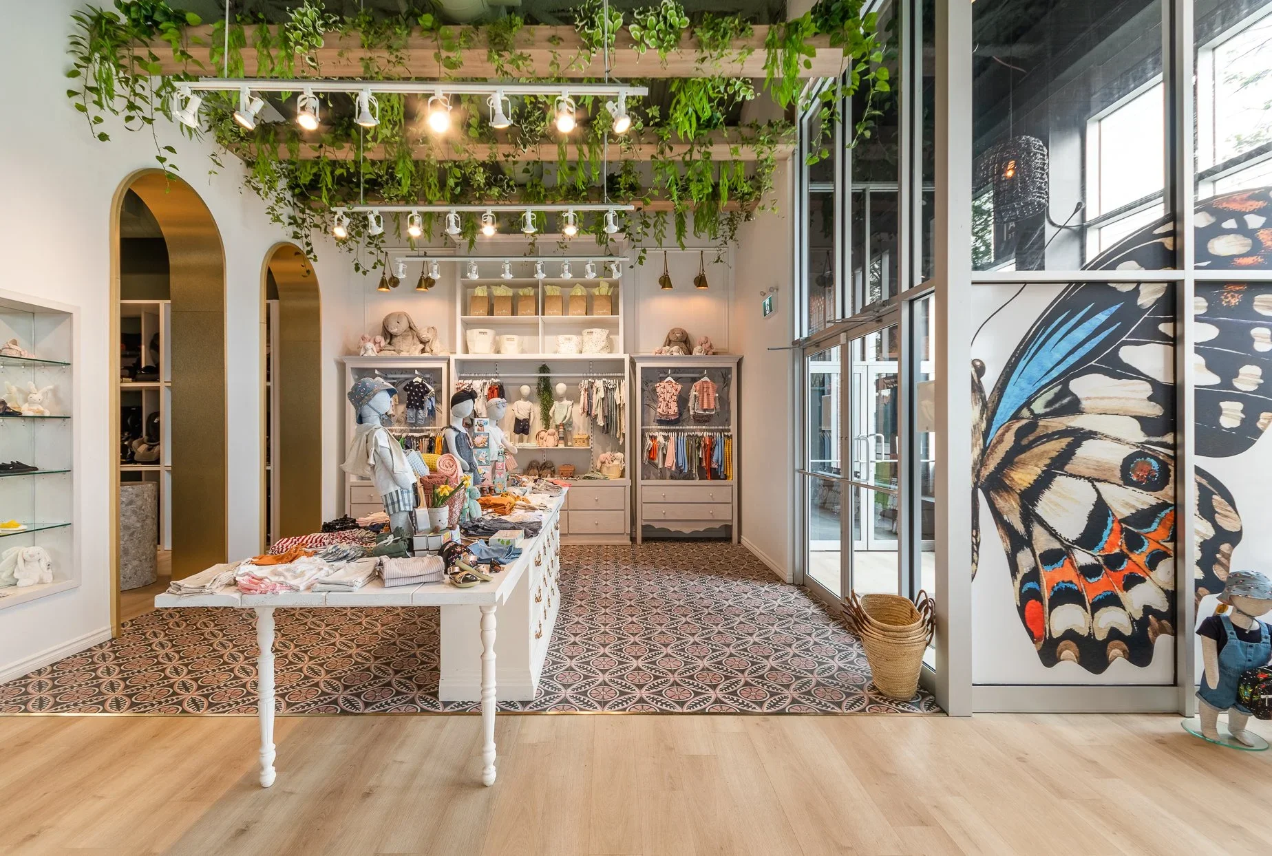 Boutique pour enfants Agatha conçue par RÜBIK DESIGN : arches, plantes suspendues, grande murale de papillon et carrelage à motifs