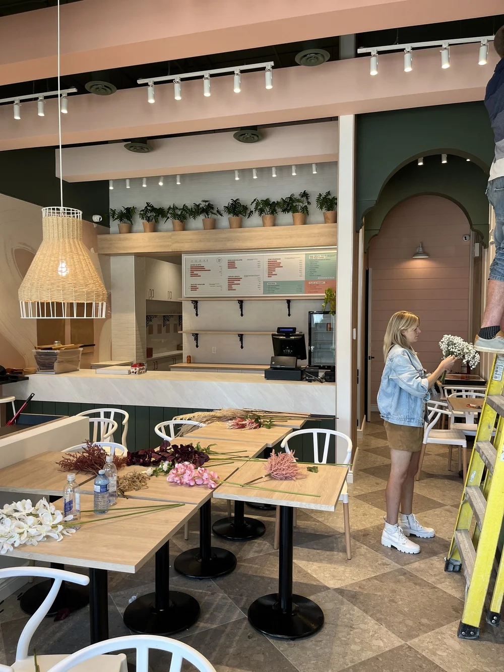 Une jeune femme dans un café ou restaurant, portant un manteau jean décontracté et une jupe courte tient un bouquet de fleurs blanches pour la décoration finale d'un projet commercial.