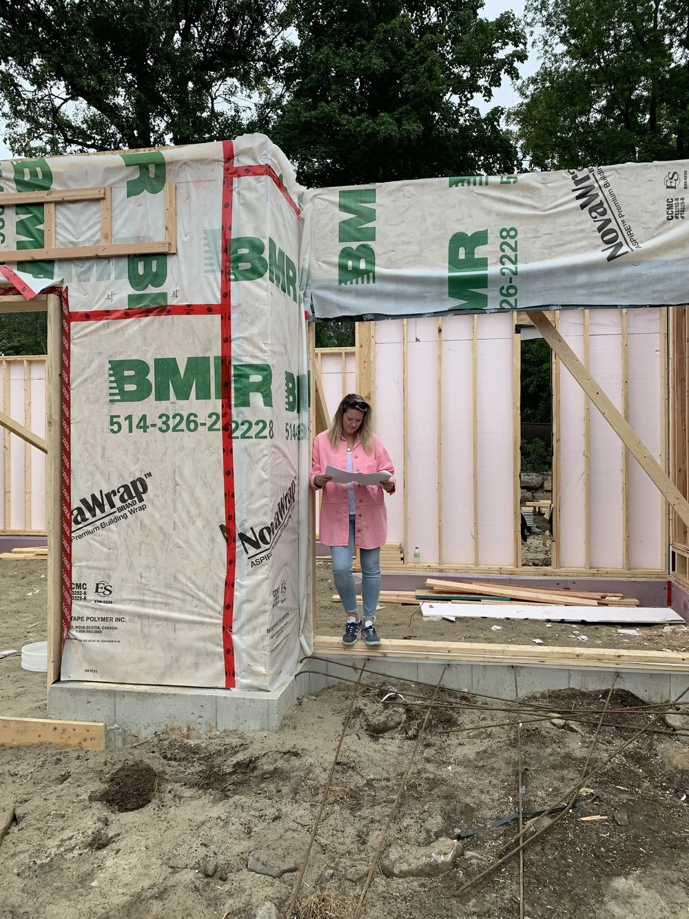Sophie Roy, propriétaire et designer intérieur, pose dans l'entre-porte d'un projet résidentiel en construction, entourée de structures en bois et de matériaux de construction.