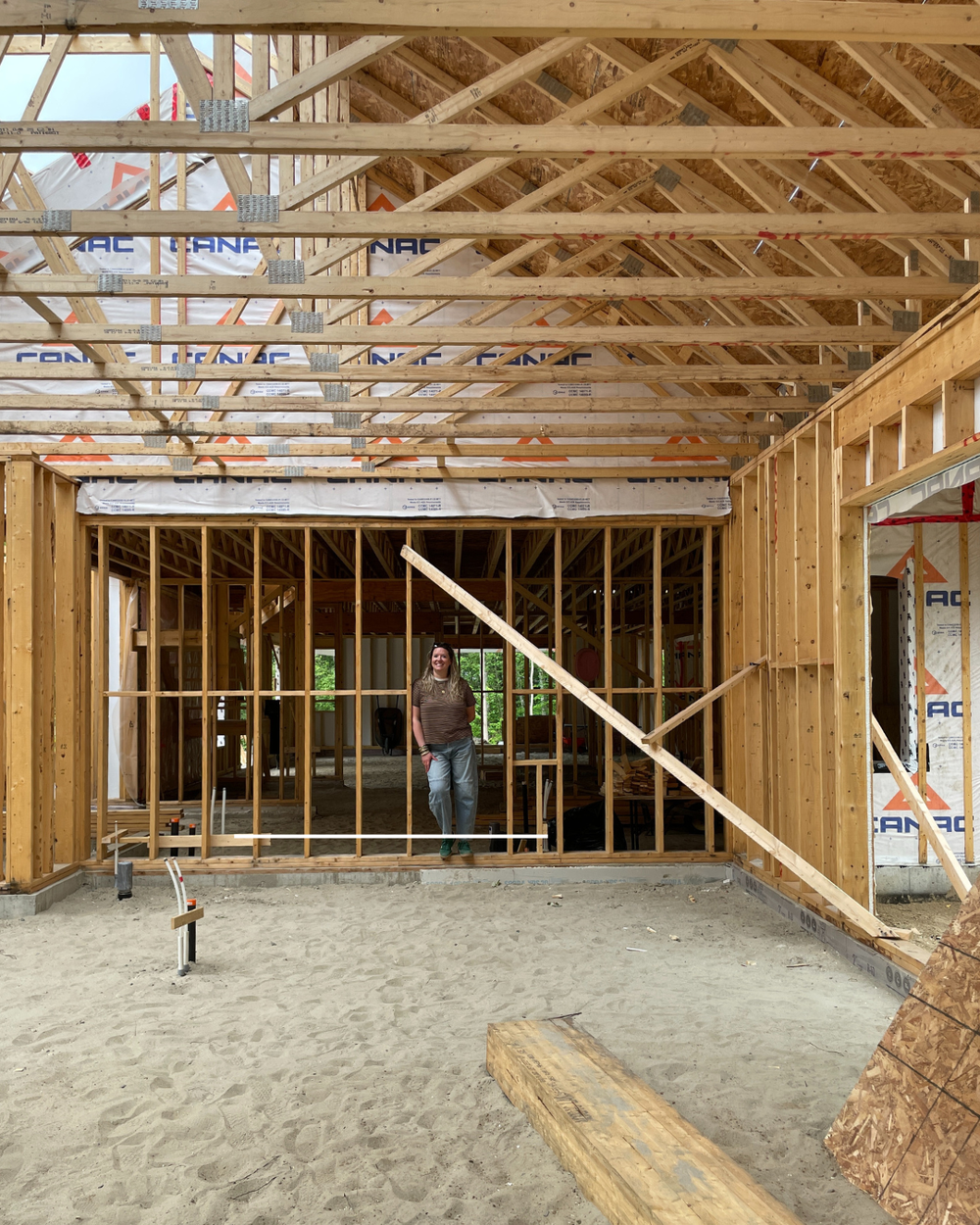 Structure de construction d'une maison avec une structure partielle en cours de réalisation et en bois visible, sol en terre et Sophie Roy, propriétaire et designer d'intérieur chez Rubik Design à Laval.