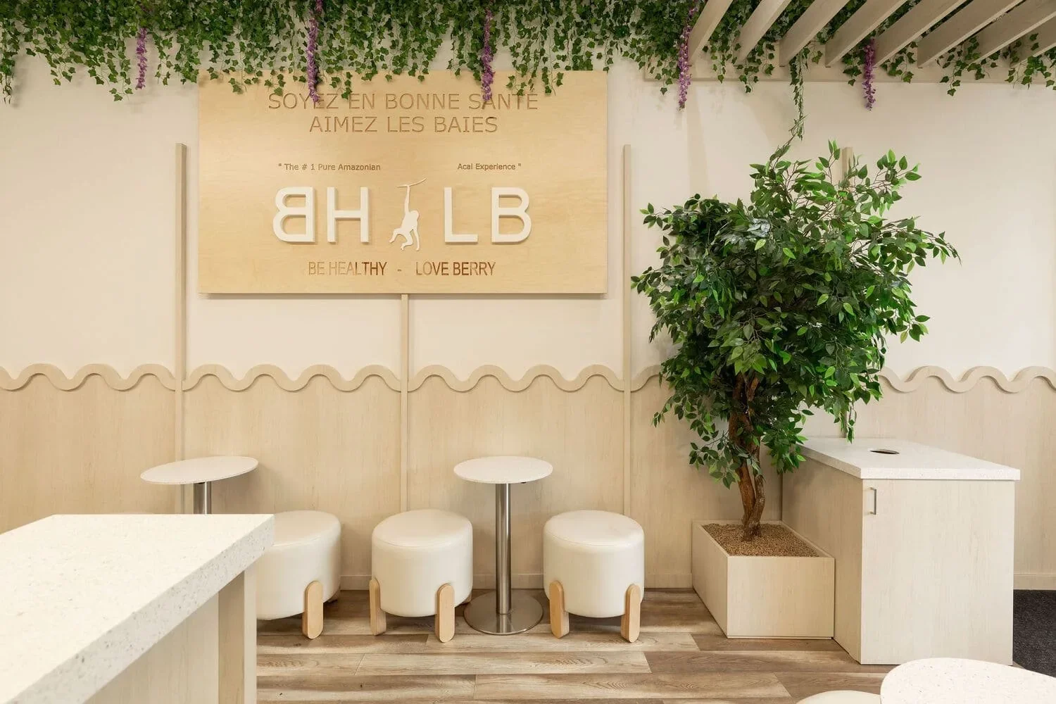 Comptoir du café Be Healthy Love Berry en Rive-Nord par Rübik Design : enseigne en bois, ficus, tabourets crème et mur à motif ondulé