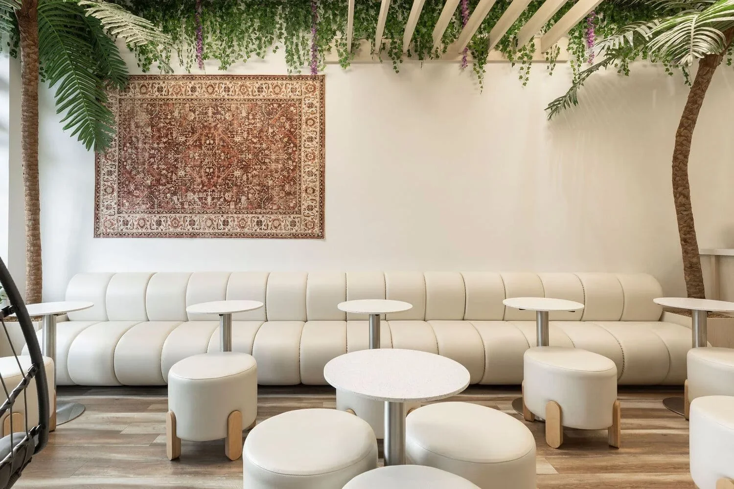 Salle du café Be Healthy Love Berry en Rive-Nord par Rübik Design : banquette crème, tapis mural persan, palmiers et plafond à lattes