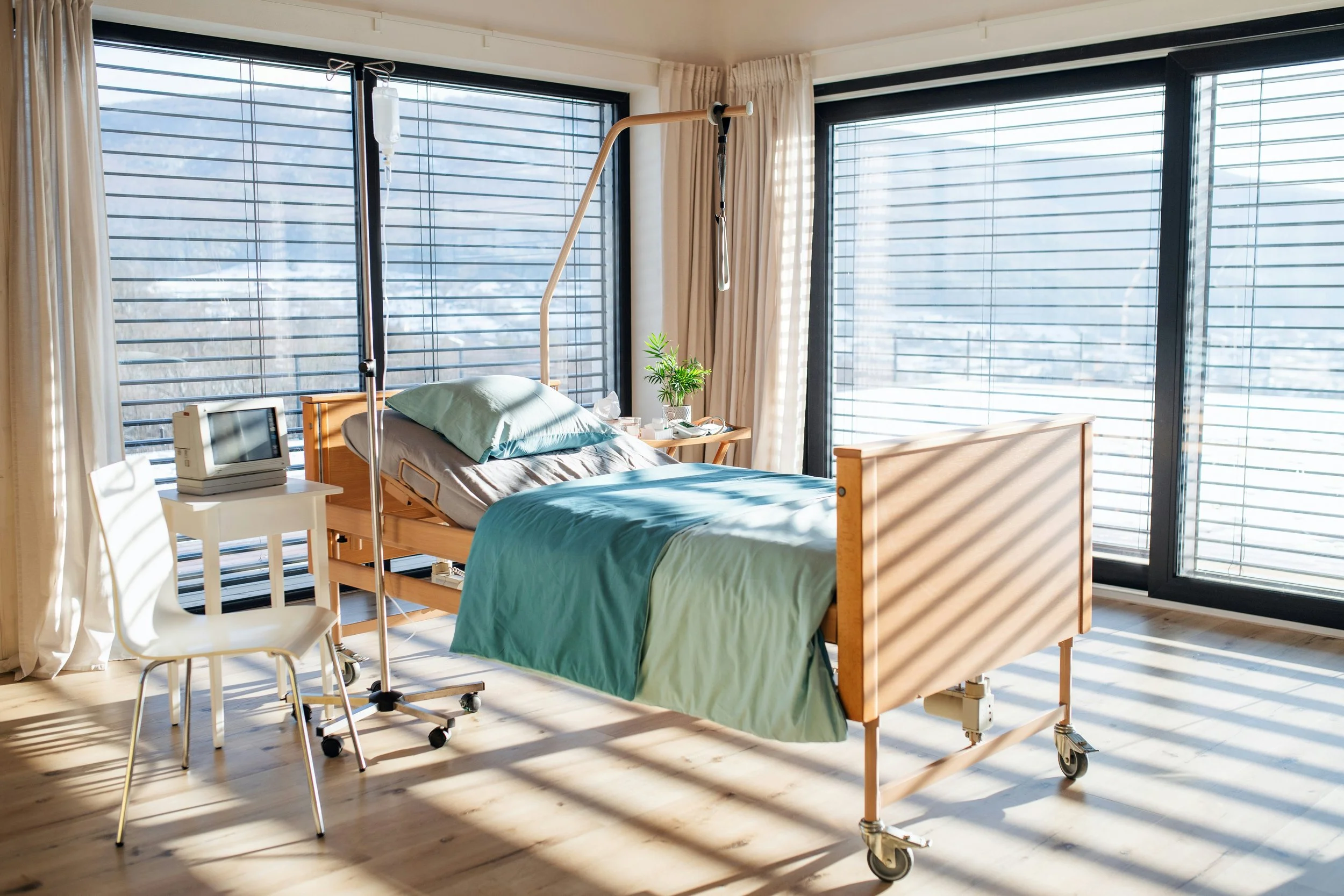 Chambre de soins lumineuse avec lit médicalisé en bois, literie verte et grandes fenêtres ensoleillées 