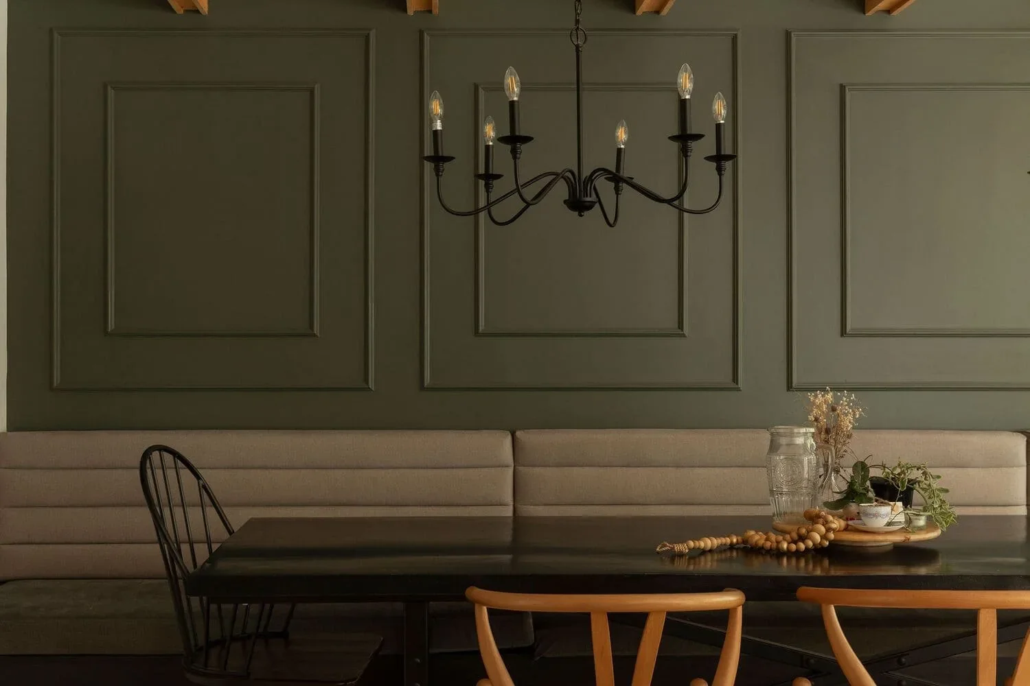 Salle à manger d'une maison de la Rive-Nord par Rübik Design : boiseries vert olive, banquette beige, lustre à chandelles et chaises en bois