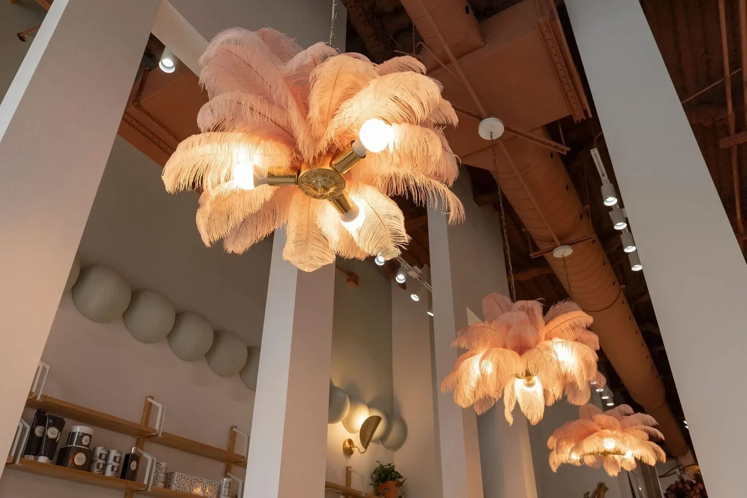 Design d’intérieur d’une boutique beauté à Montréal par Rübik Design : luminaires en plumes roses, colonnes blanches et étagères en bois