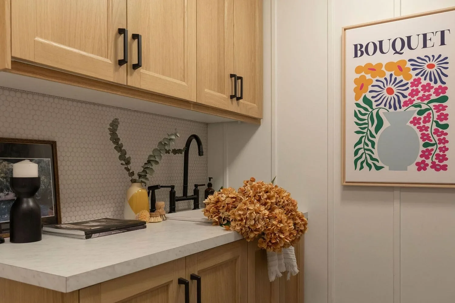 Cuisinette d'un sous-sol rénové à Montréal par Rübik Design : armoires en chêne, dosseret en mosaïque hexagonale et affiche florale