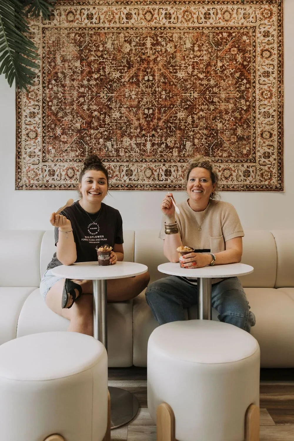 Deux clientes attablées dans le café Be Healthy Love Berry en Rive-Nord par Rübik Design : banquette crème, tabourets rembourrés et tapis mural persan