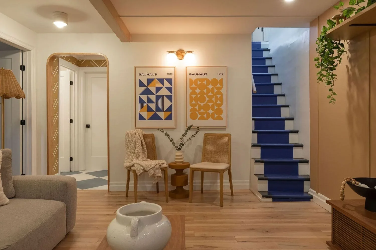 Sous-sol rénové à Montréal par Rübik Design : arche en bois, chaises cannées, affiches Bauhaus et escalier peint en bleu