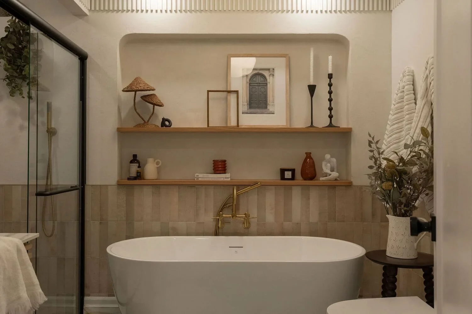 Salle de bain rénovée à Montréal par Rübik Design : bain autoportant, niche arrondie avec tablettes en bois et robinetterie dorée