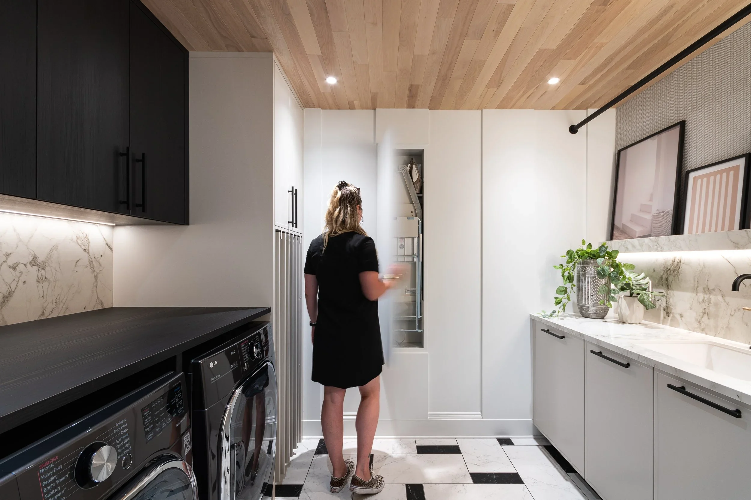 Salle de lavage rénovée avec ébénisterie blanche sur mesure, plafond de bois et plancher damier noir et blanc