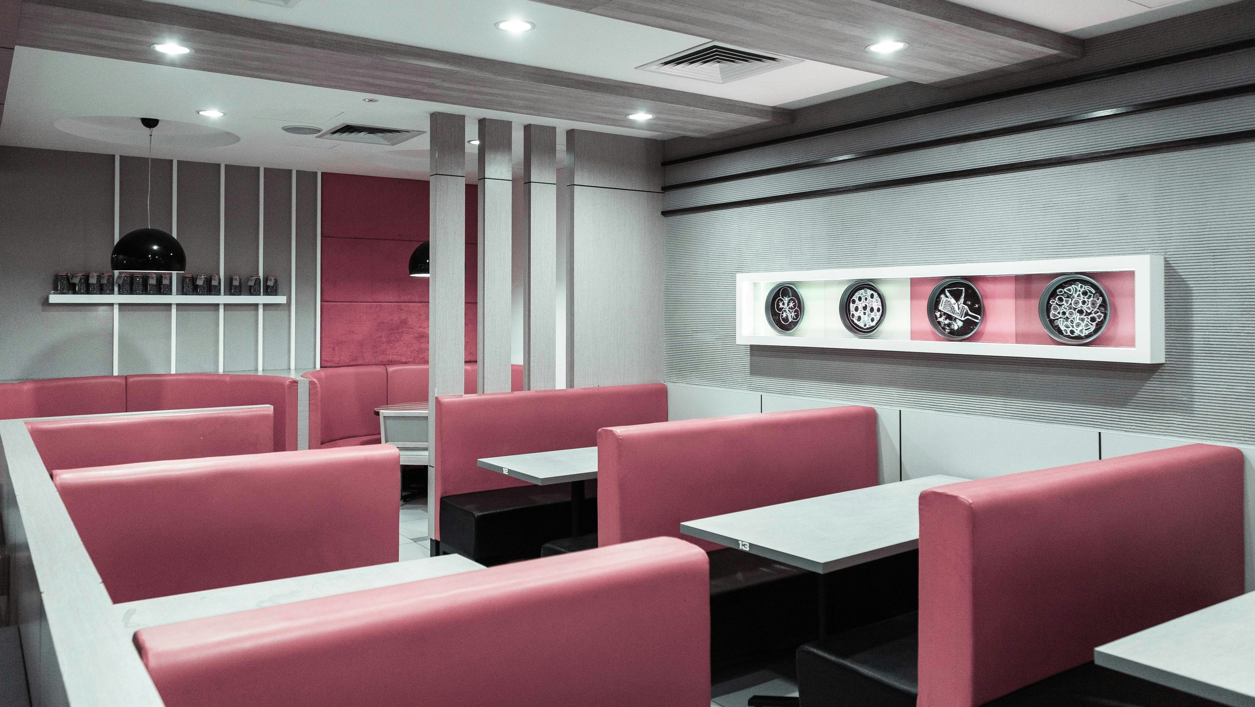 Salle à manger de restaurant avec banquettes capitonnées roses, tables blanches et éclairage encastré doux 