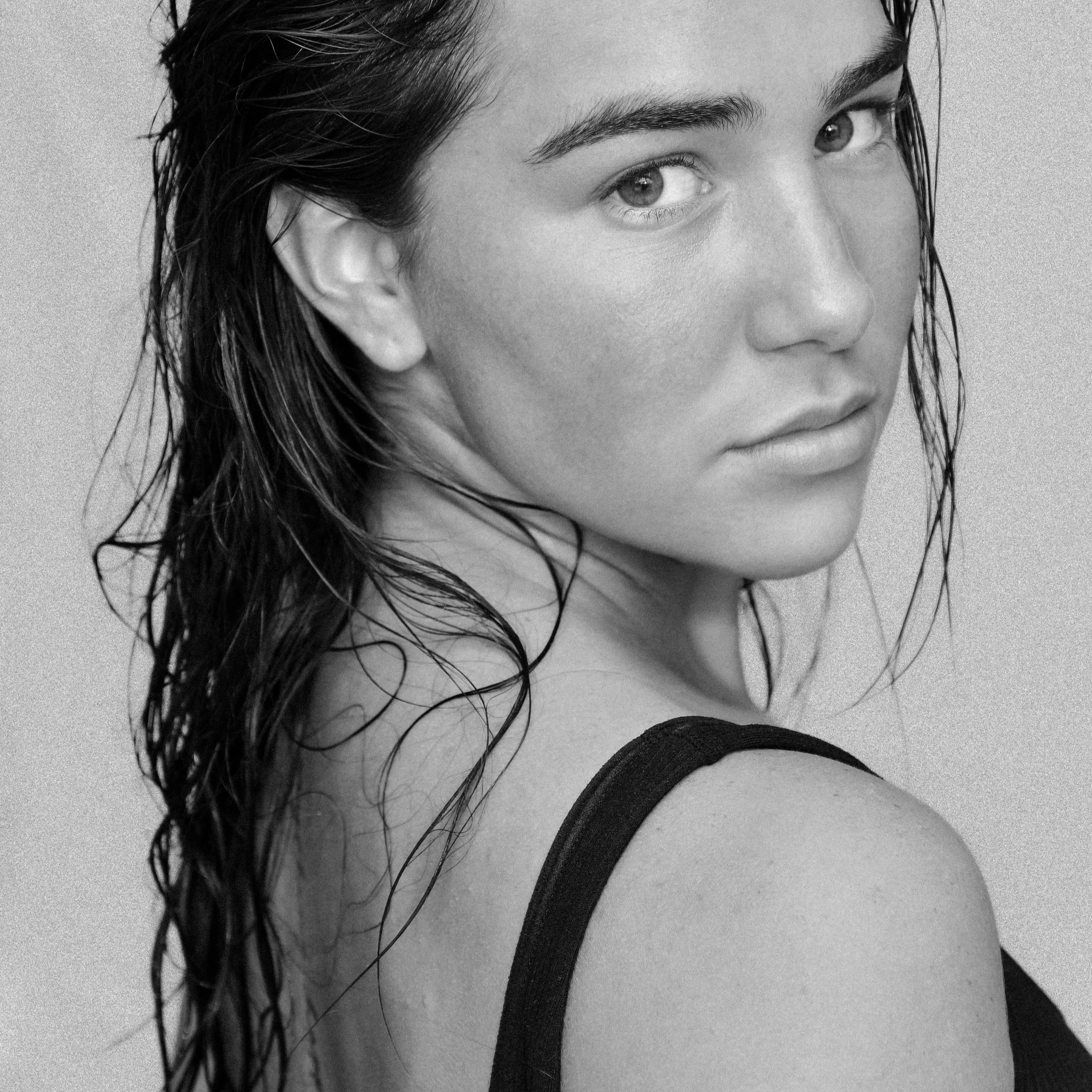 Close-up black and white photo of a woman's face, showing her left eye, eyebrow, and part of her nose and lips, with wet hair falling over her face.