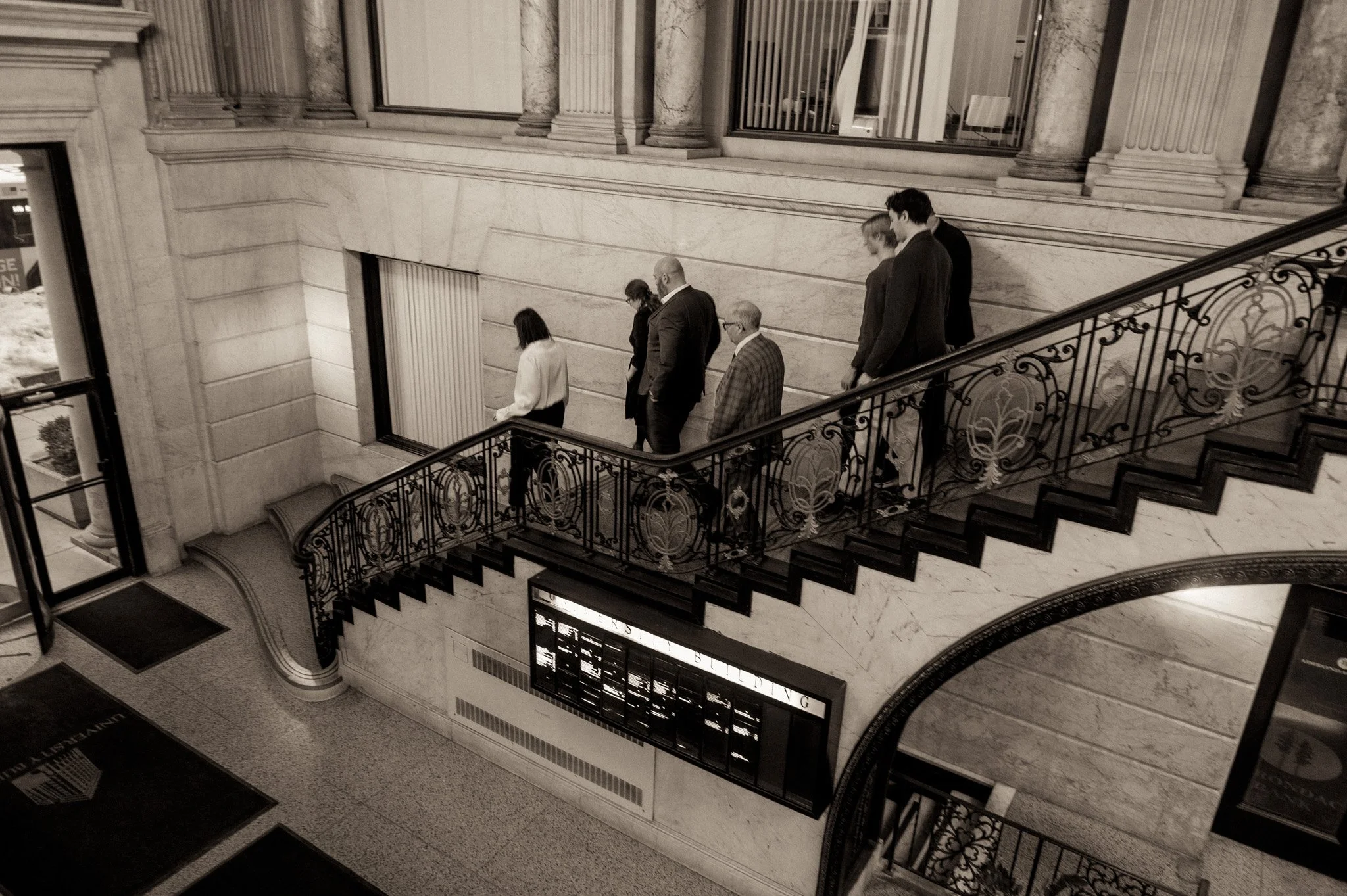 People walking down a marble staircase in a building with classic architectural details.